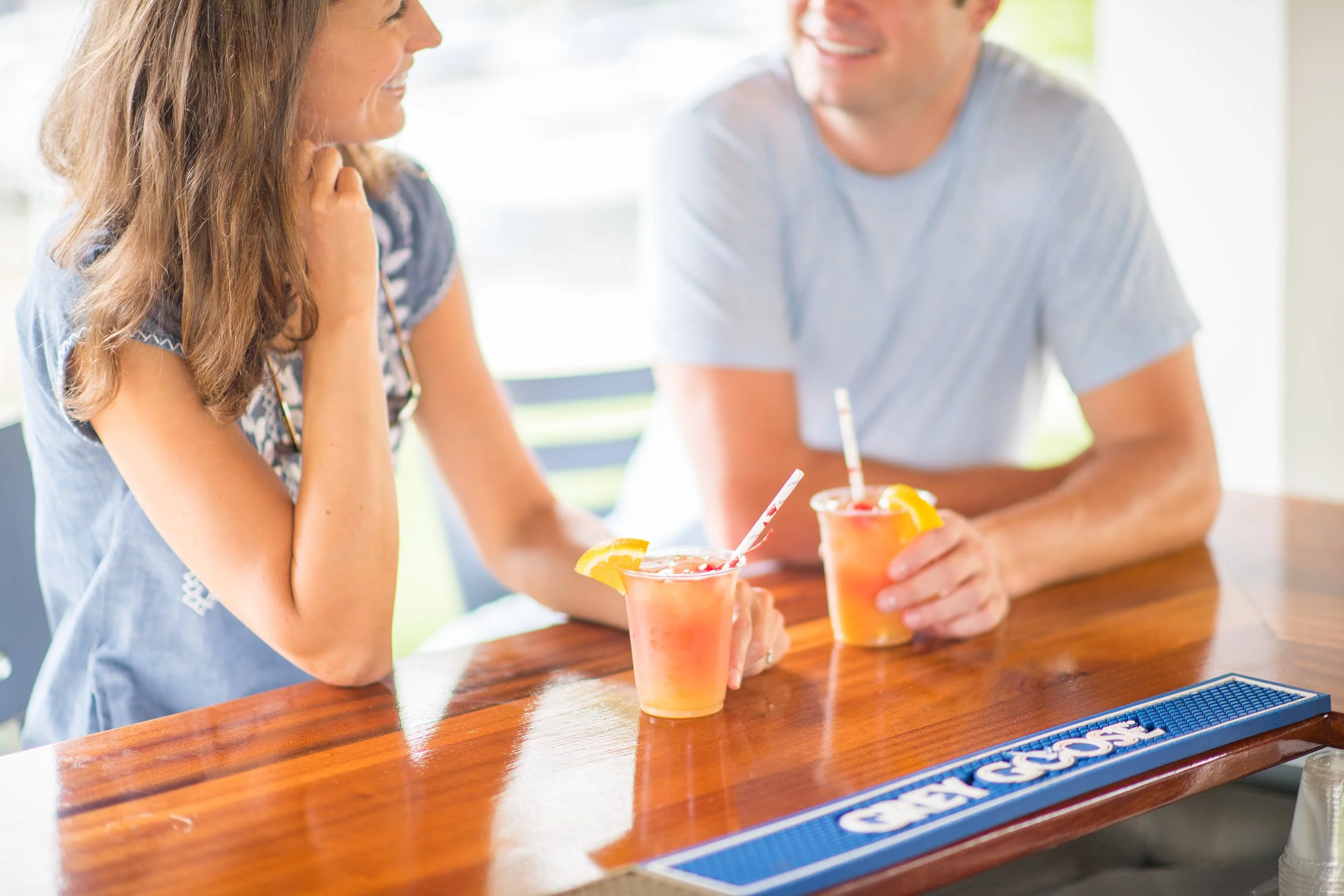 boyfriend and girlfriend smiling at each other while enjoying a cocktail at an outdoor bar in vermont