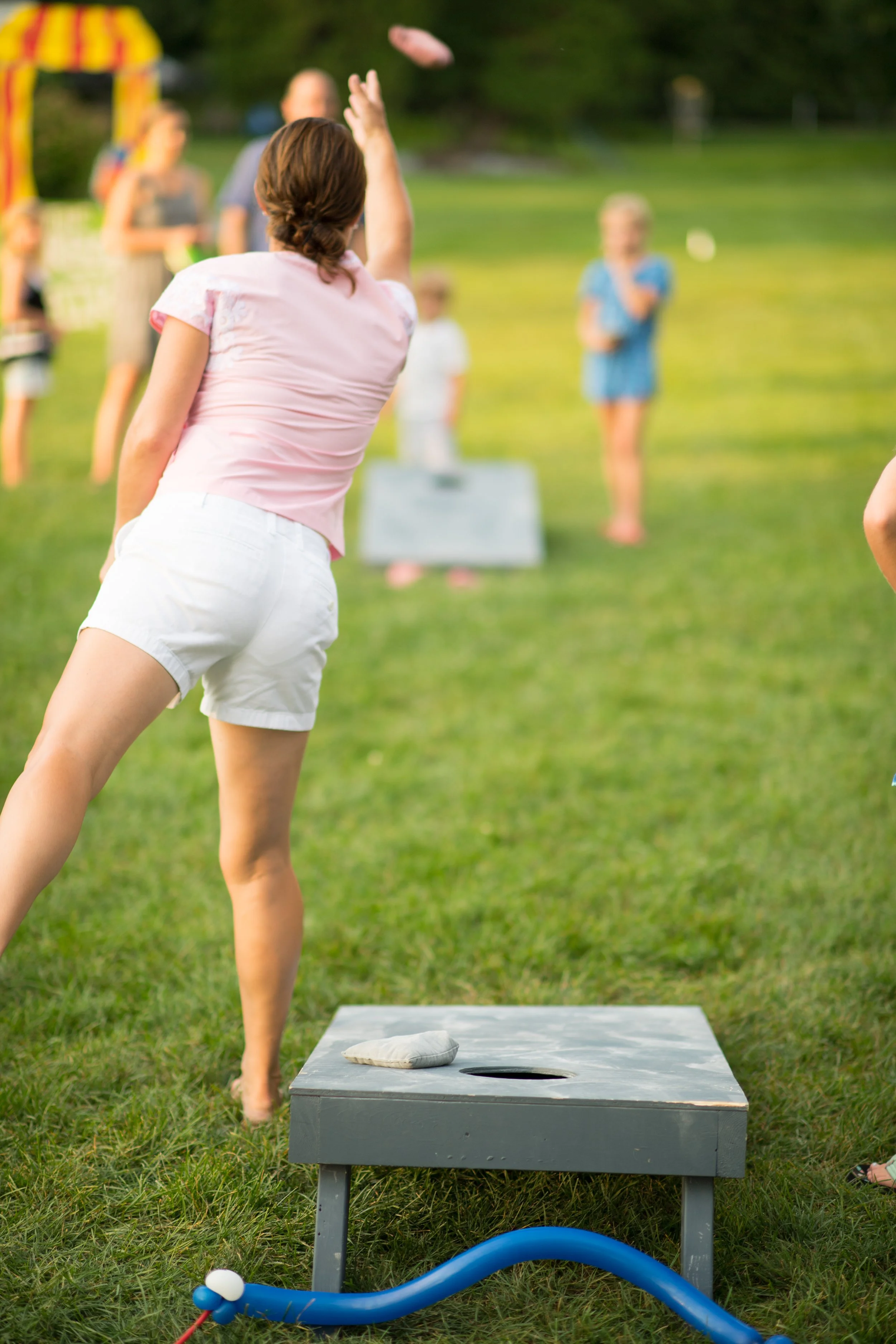 a mother throws a sandbag at the target while playing cornhole with her kids