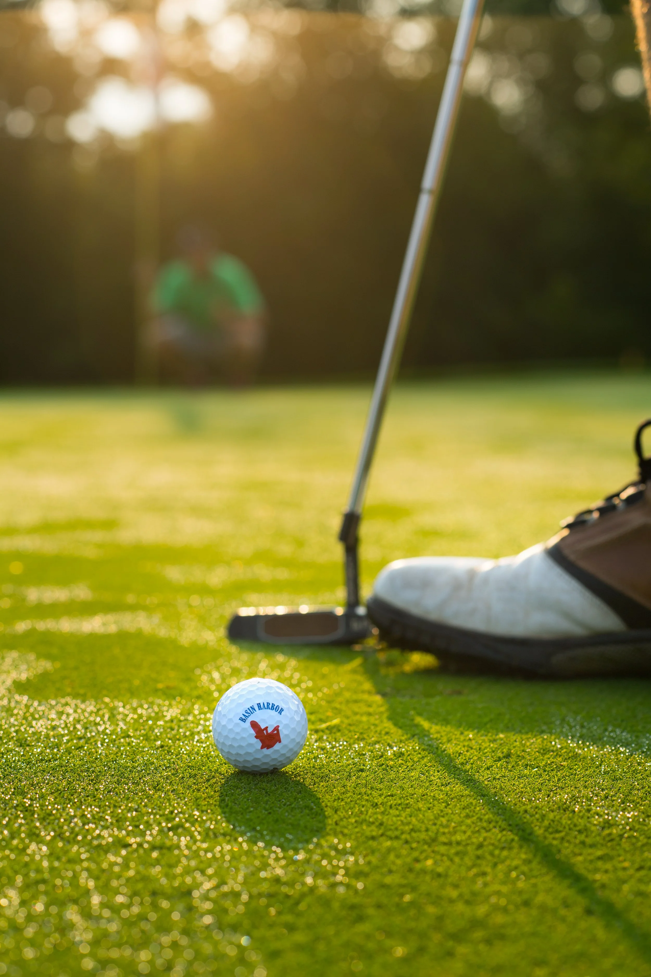 a golf ball in the foreground as a golfer gets ready to putt on a dewey green at basin harbor vermont