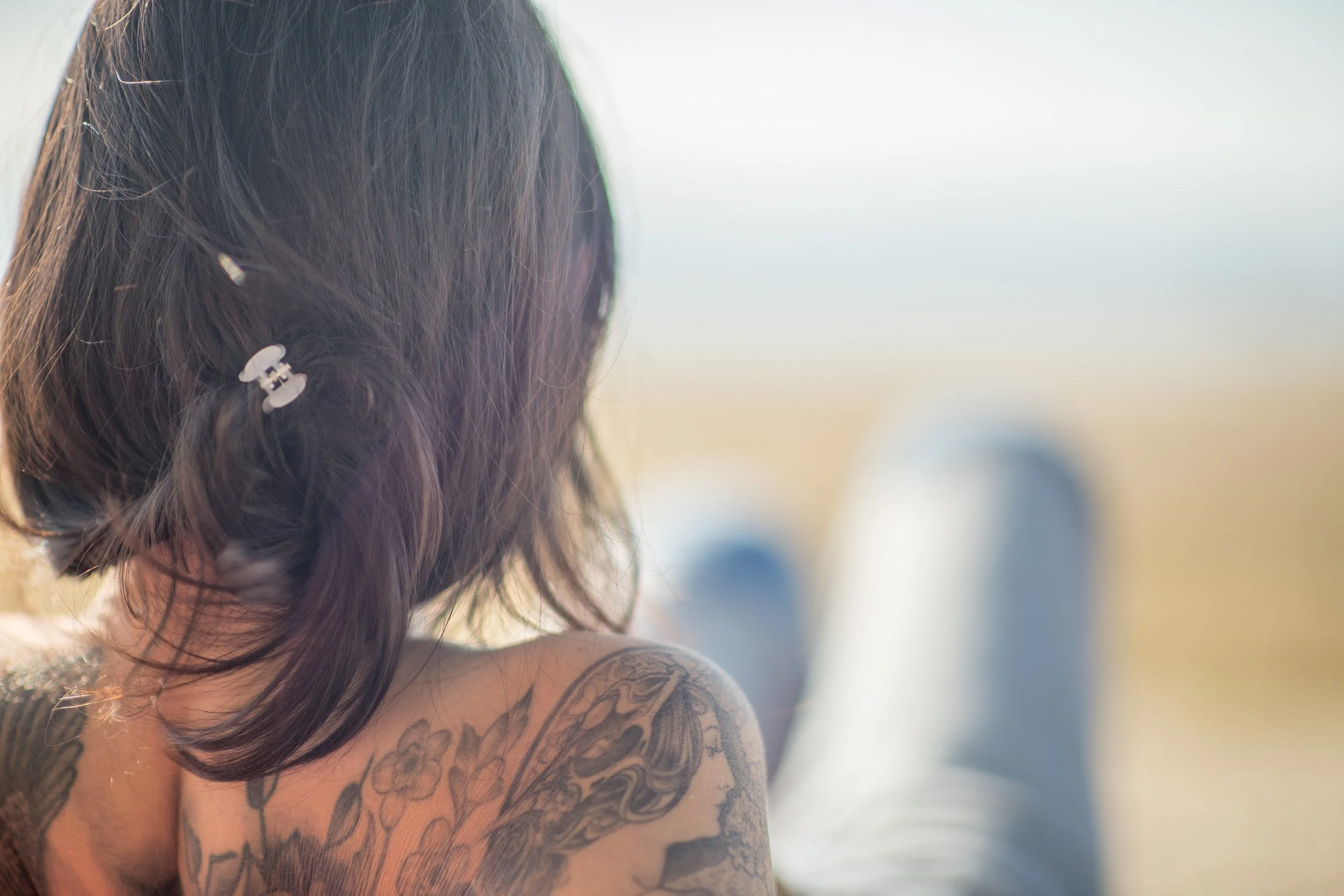 back of a womans hair and her tattooed shoulder while she sits on a beach in Burlington vt