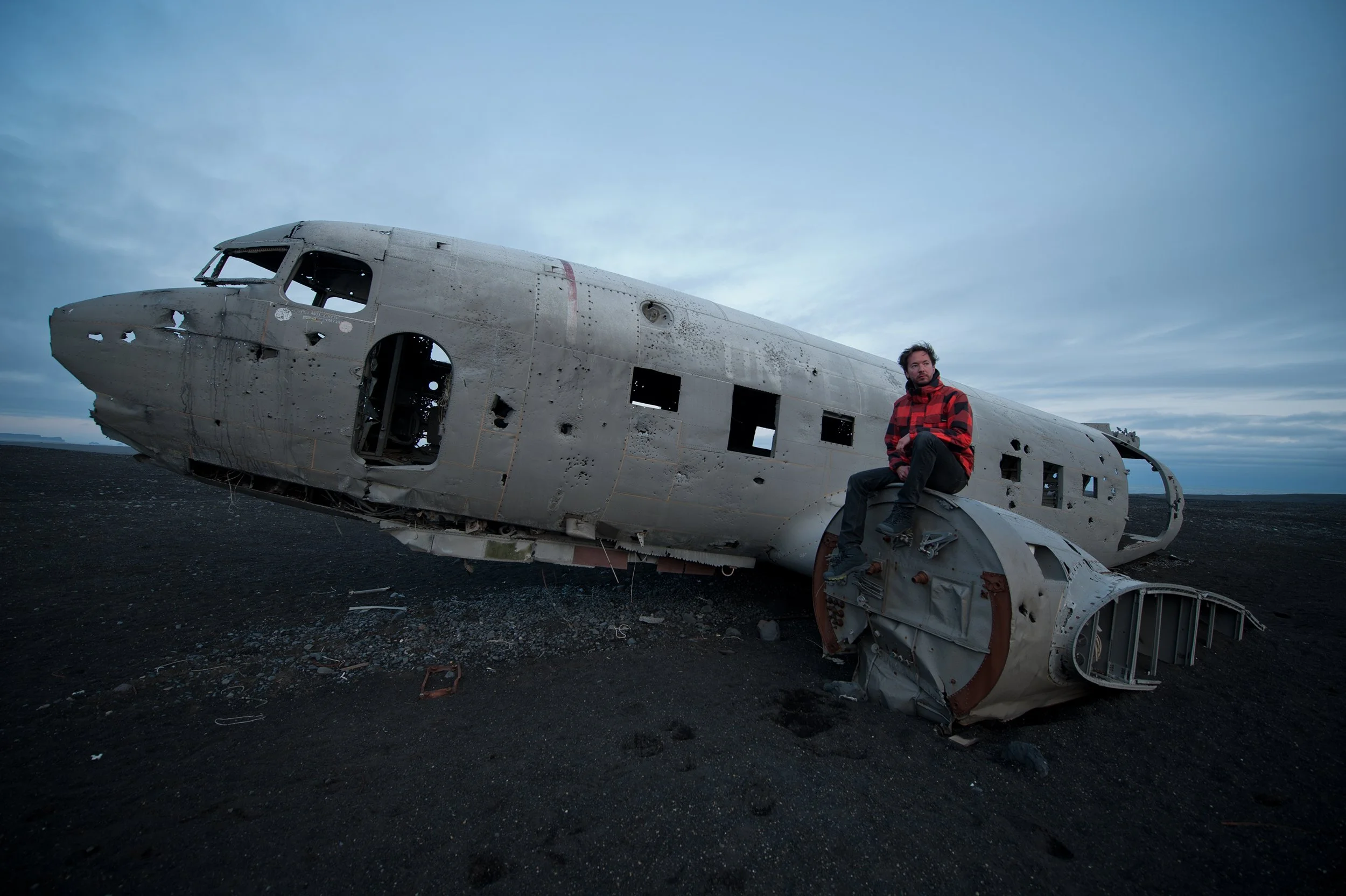 self portrait of michael heeney sitting on top of a plane wreck on a beach in iceland