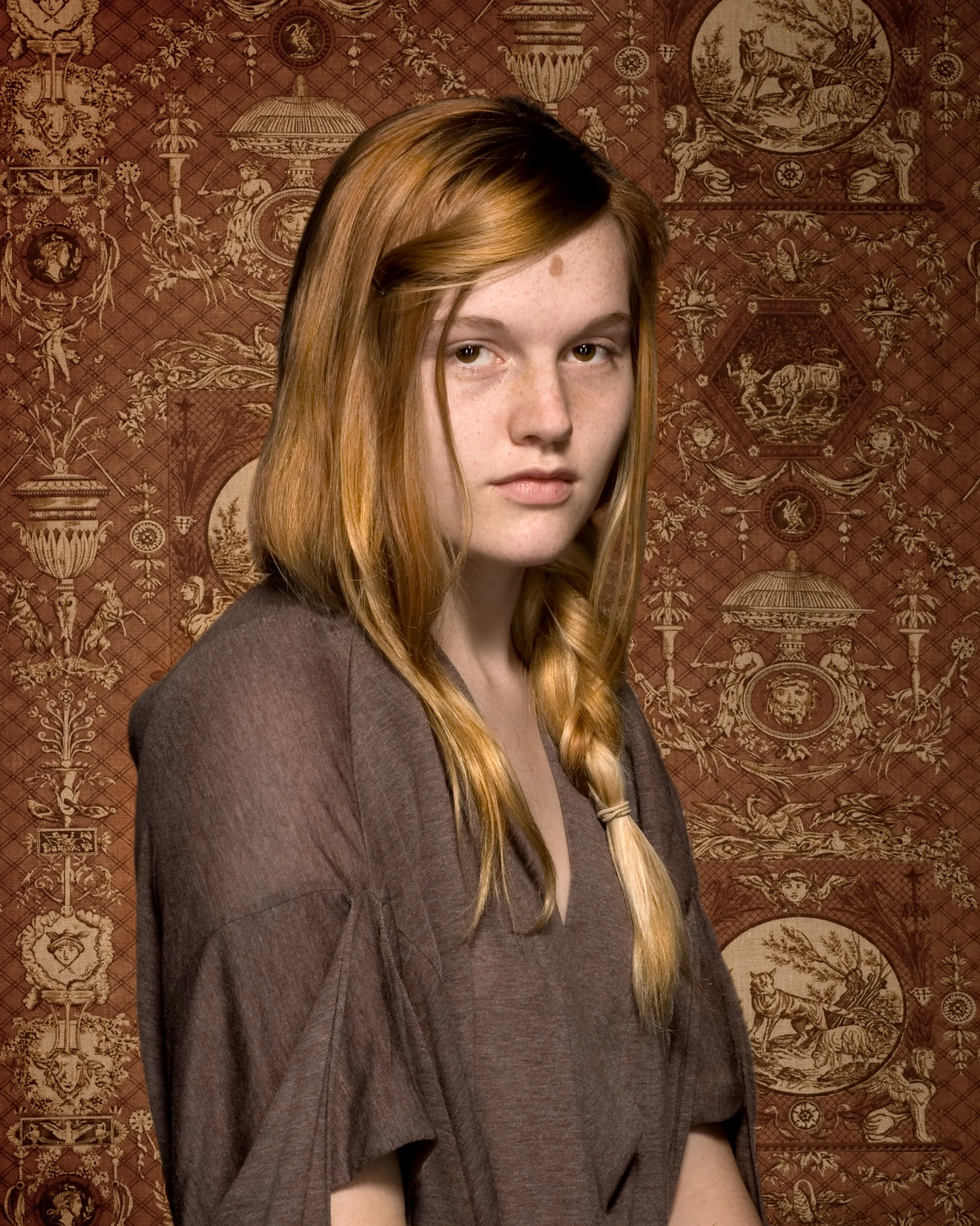 studio portrait of a red headed woman in front of damask patterned background