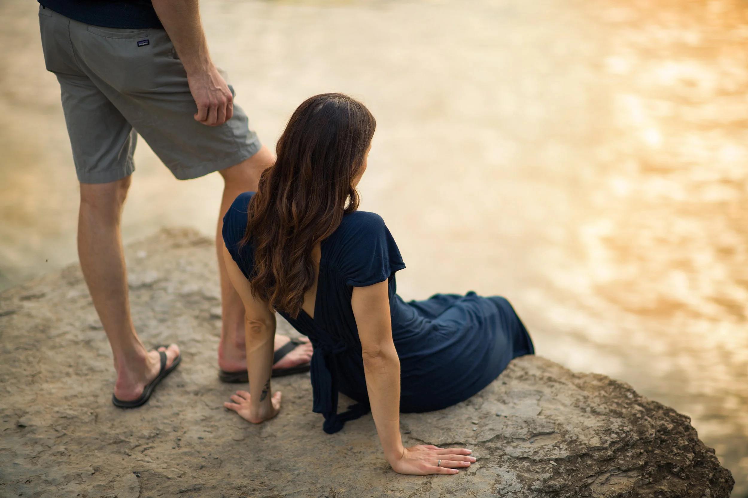 vermont lifestyle photographer image of a woman in a blue dress sitting on a rocky cliff  overlooking a lake with her boyfriend standing next to her