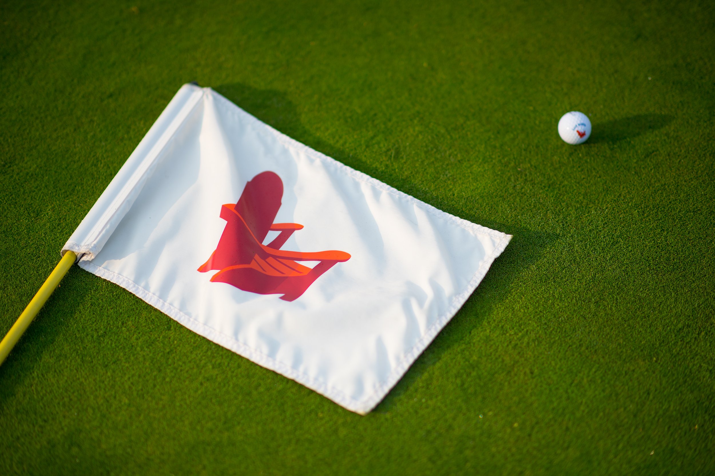 golf course flag with red adirondack chair on it laying on green with golf ball at basin harbor vt