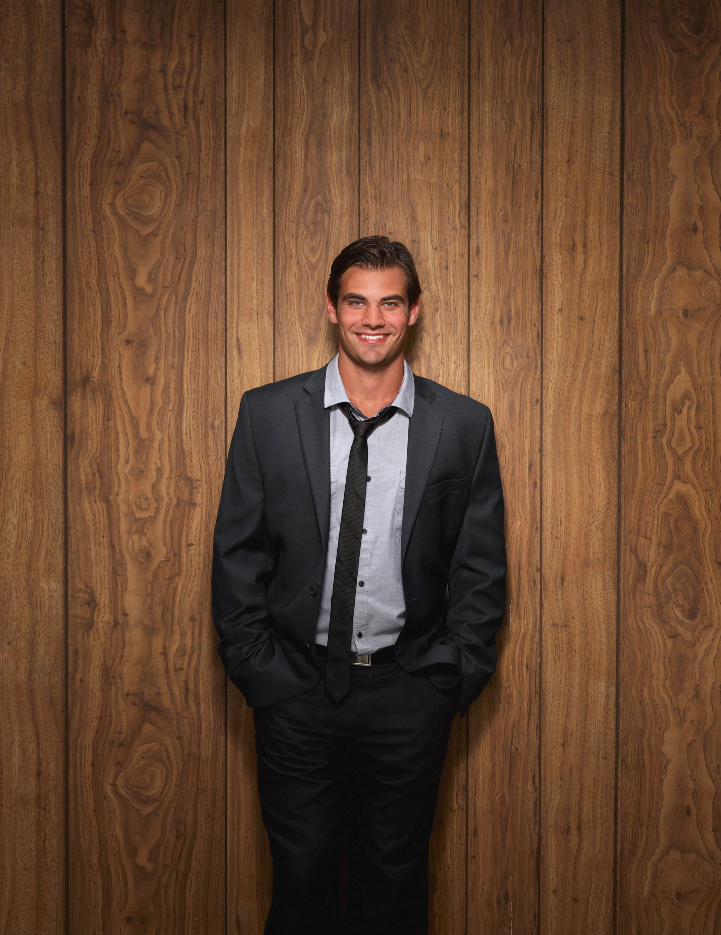 man in suit poses for a photo in front of a wood paneling background