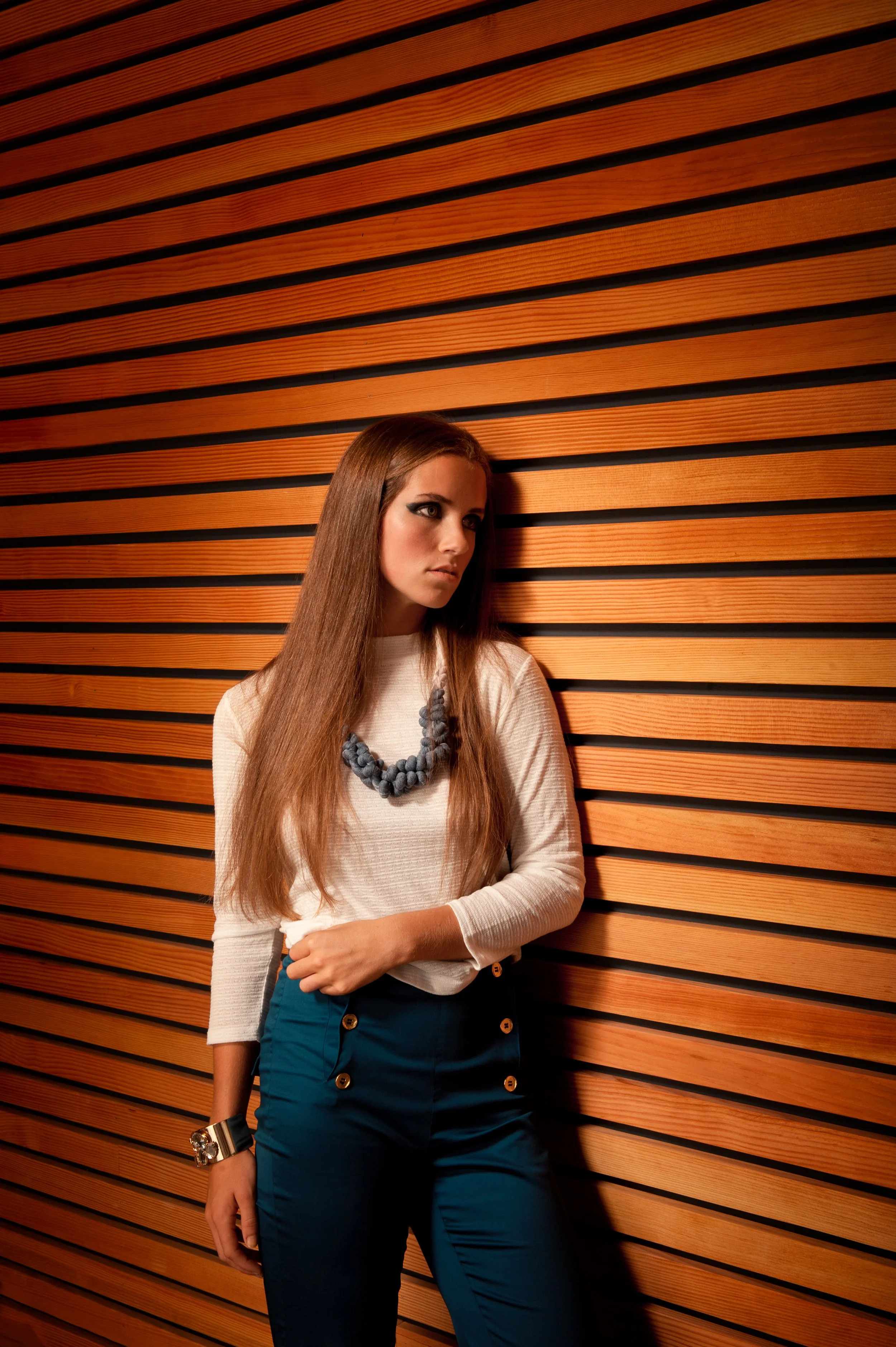 fashion photo of a woman in white top and blue pants in front of wooden slat wall