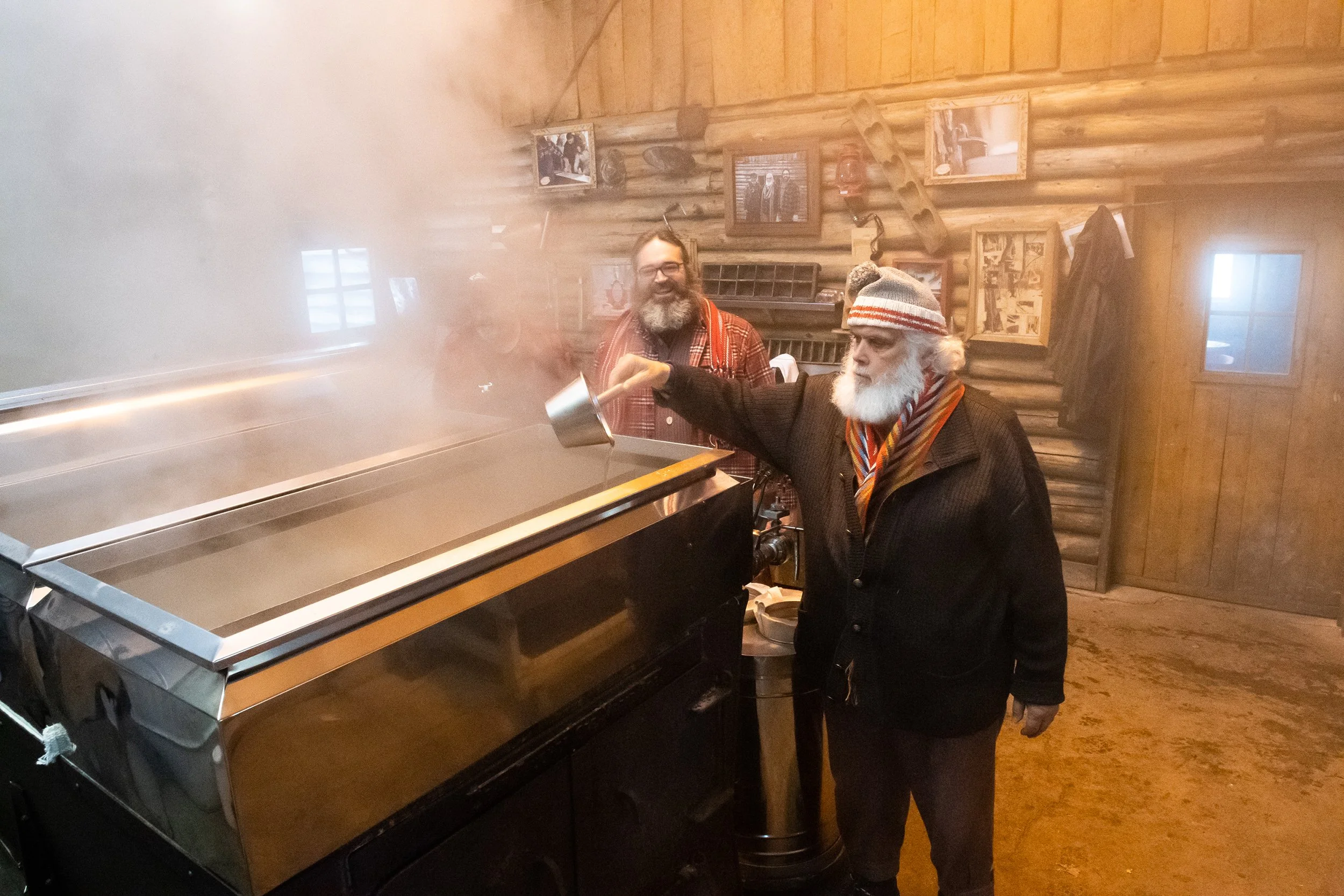 two men with big beards and red scarves test maple syrup in a sugar shack in quebec