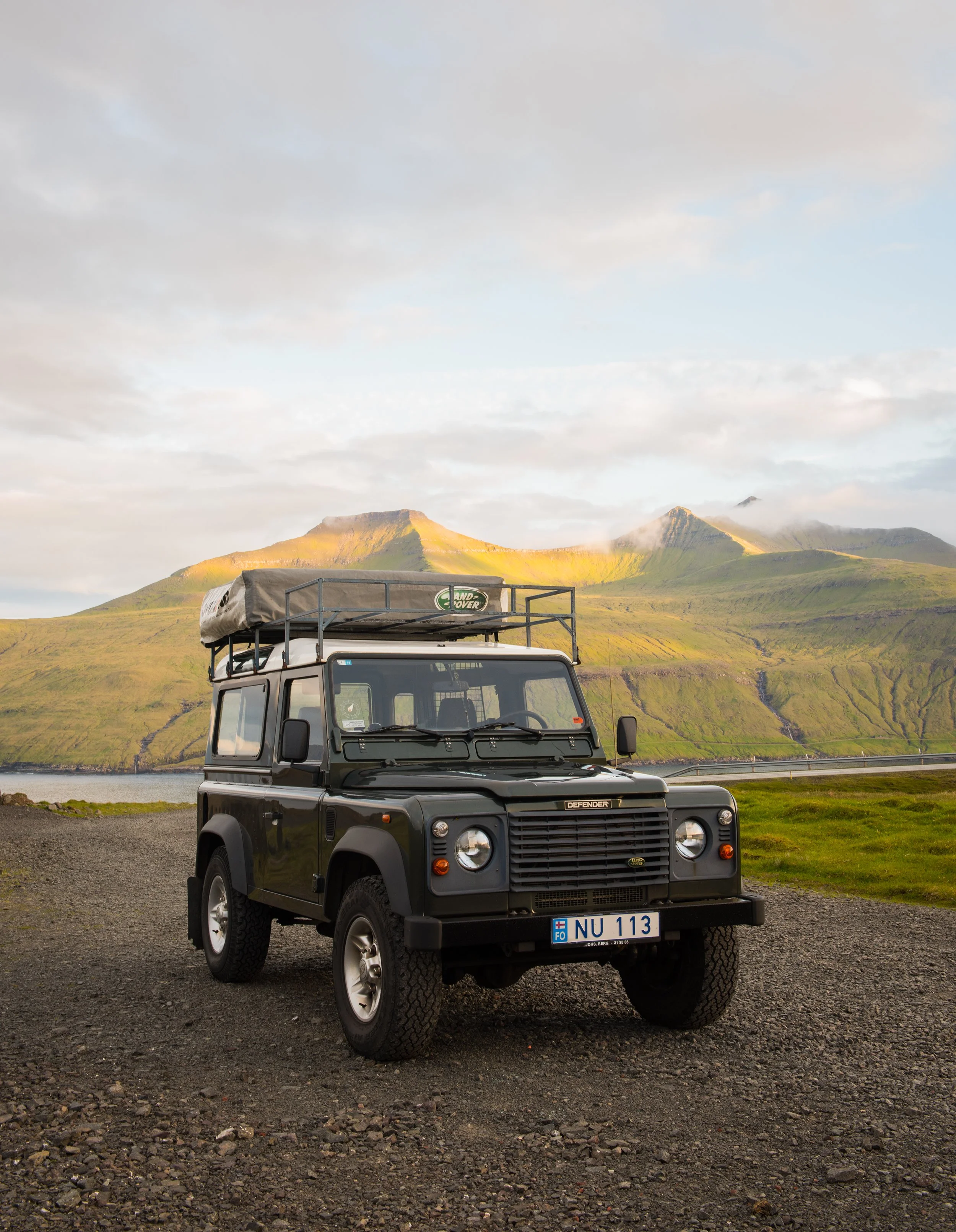 travel photography of land rover defender with rooftop tent parked in front of mountains in the faroe islands