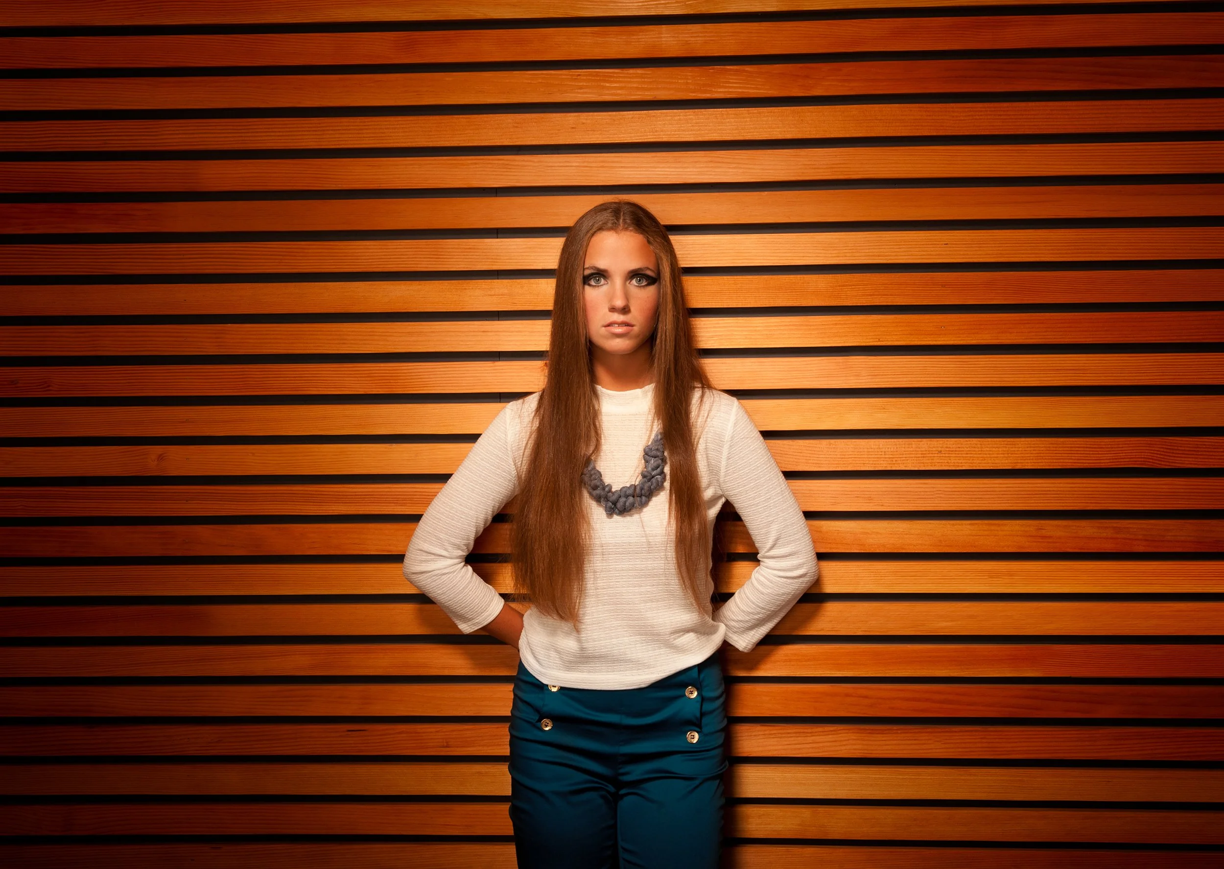 fashion photo of a woman in white top and blue pants in front of wooden slat wall