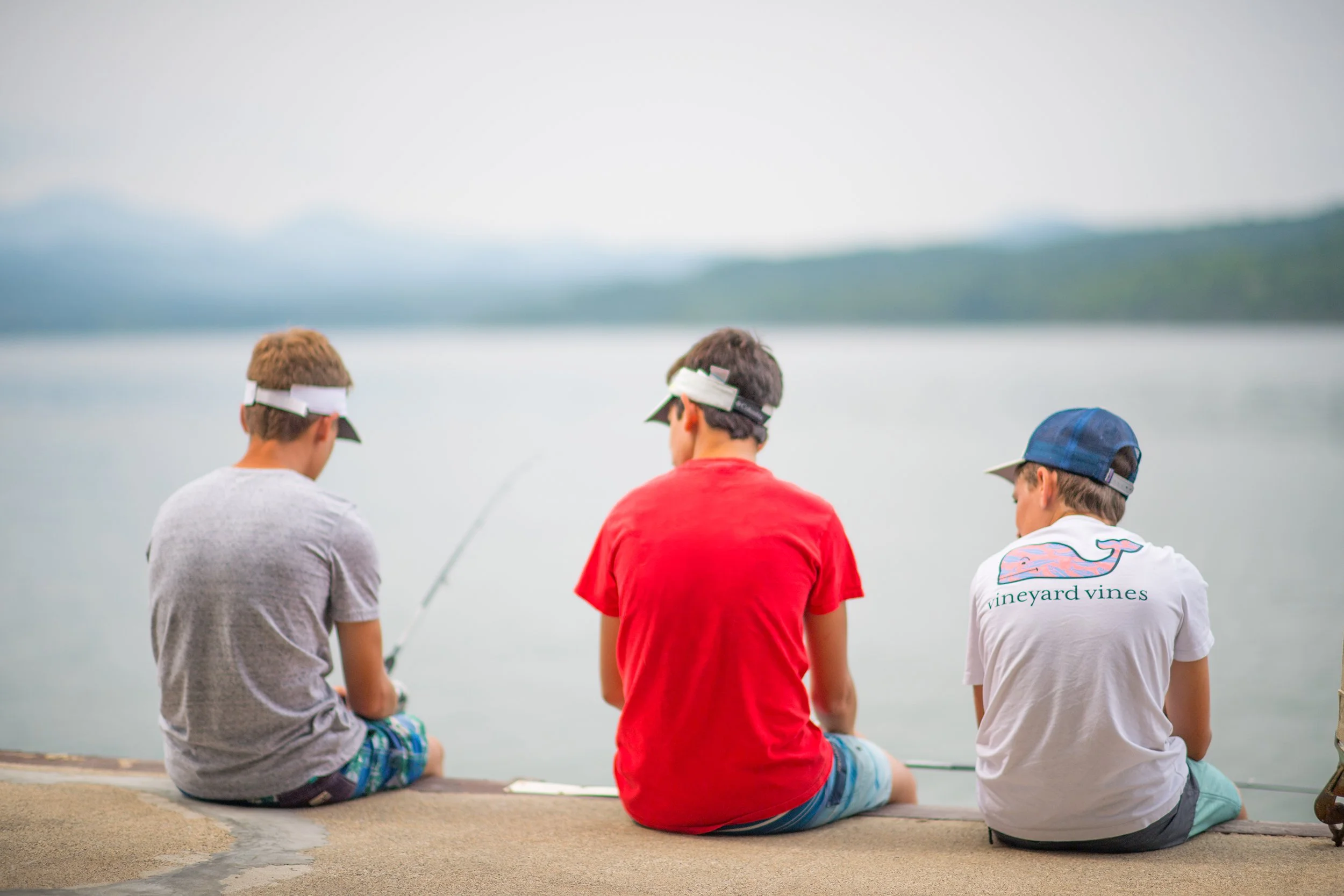 three boys sitting on a wall together while fishing in lake champlain