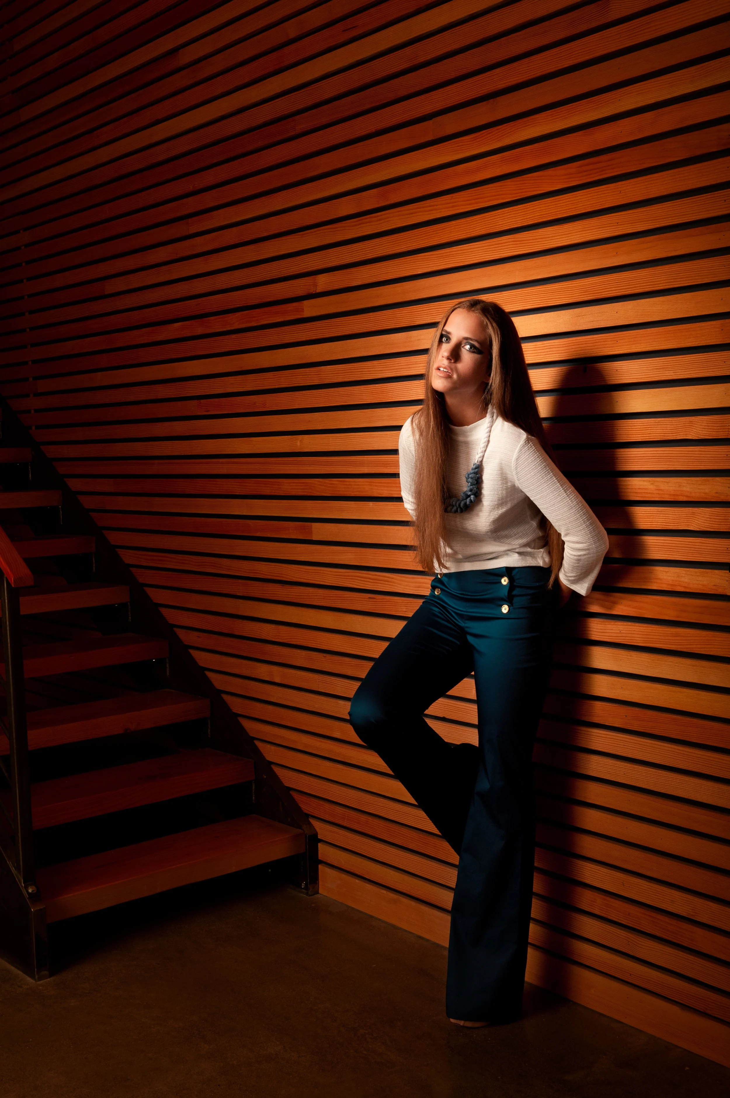 fashion photo of a woman in white top and blue pants in front of wooden slat wall