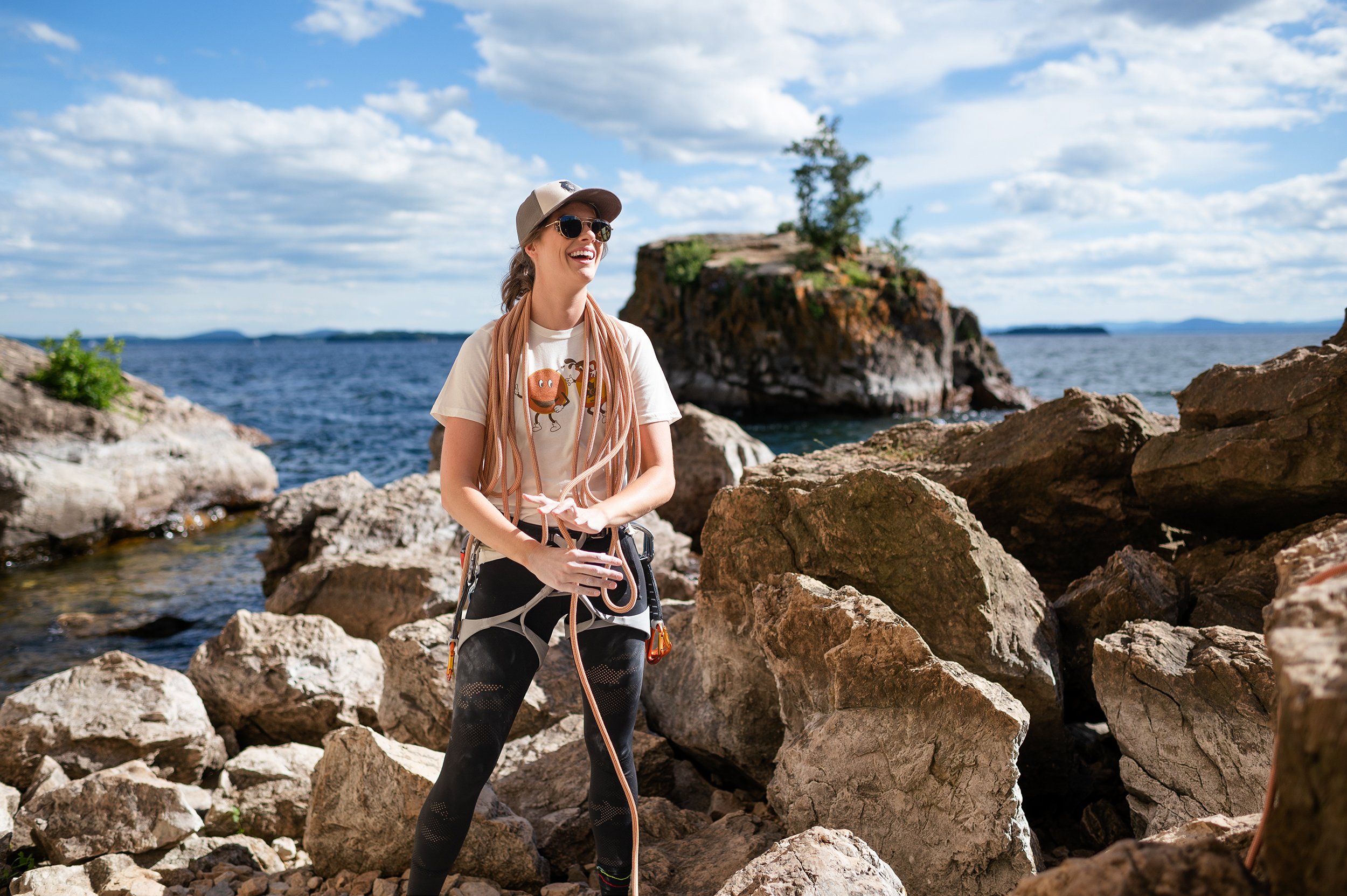 female rock climber with rope coiled over her shoulders smiles at a friend