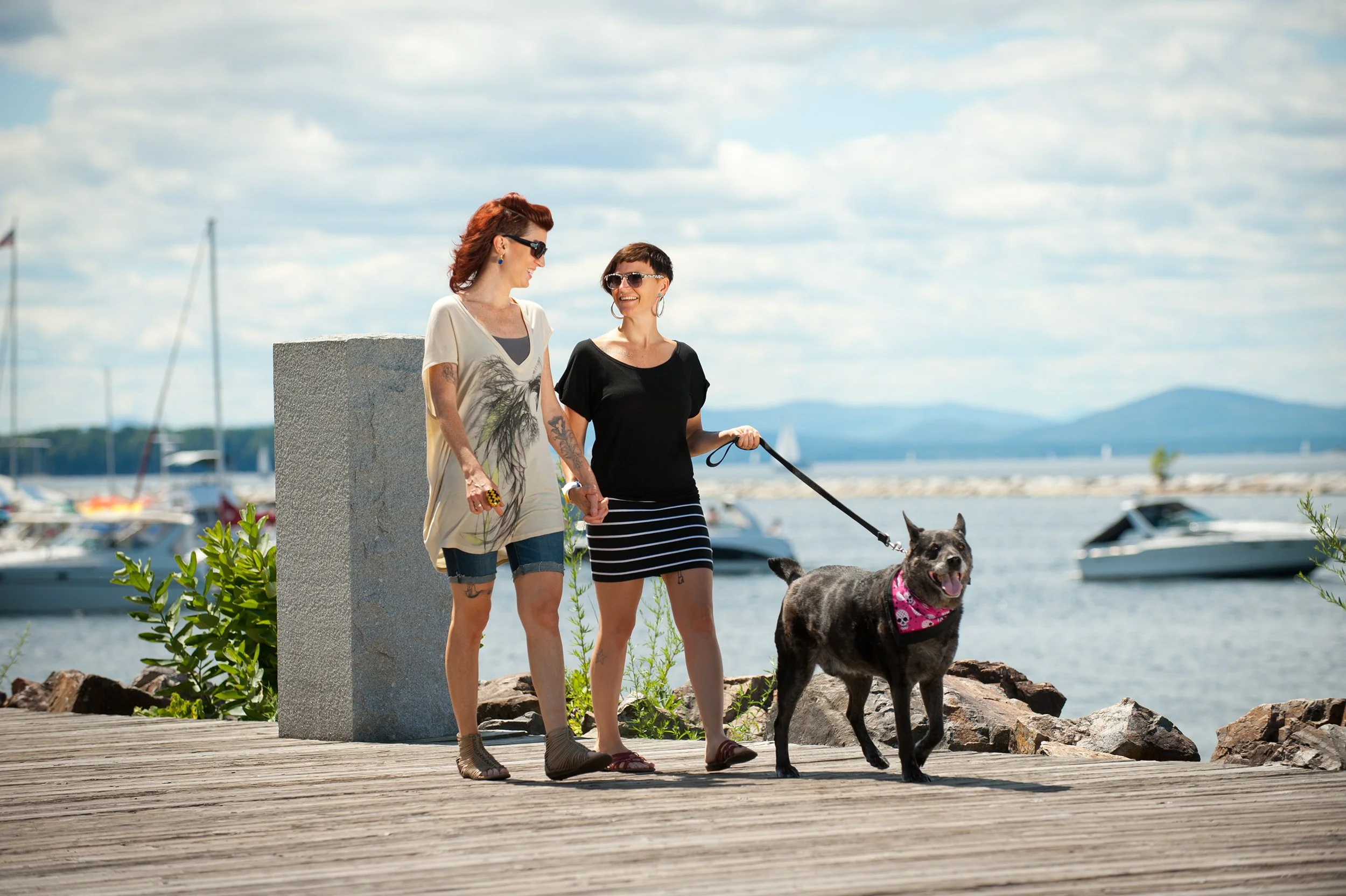 lifestyle photographer in burlington vermont captures a female couple  walking their dog on Burlington vermont's waterfront park