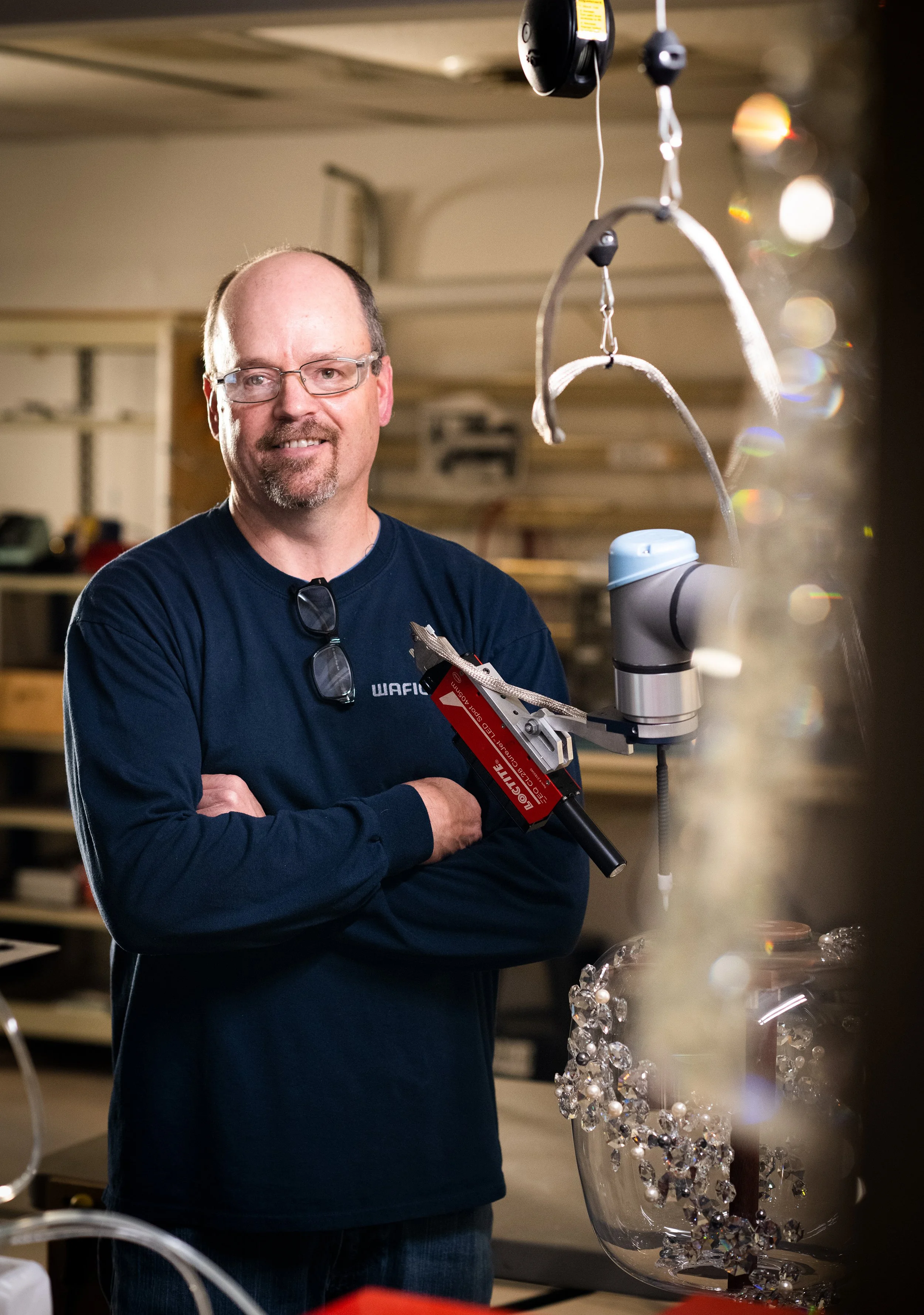 a man smiles at the camera with sparkly crystal in the foreground at schonbek lighting factory in plattsburgh new york