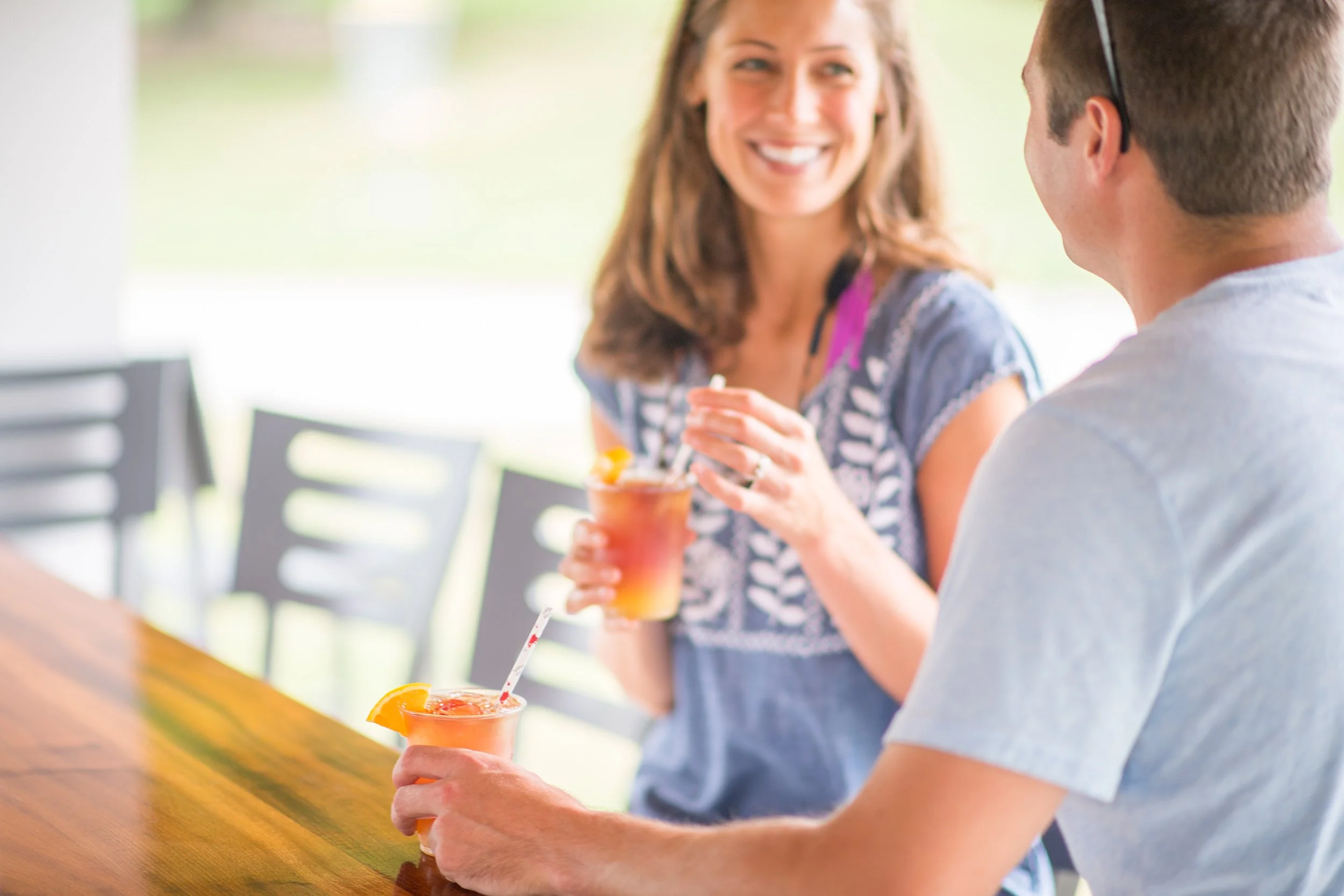 man and woman smiling at each other while enjoying a drink at an outdoor bar