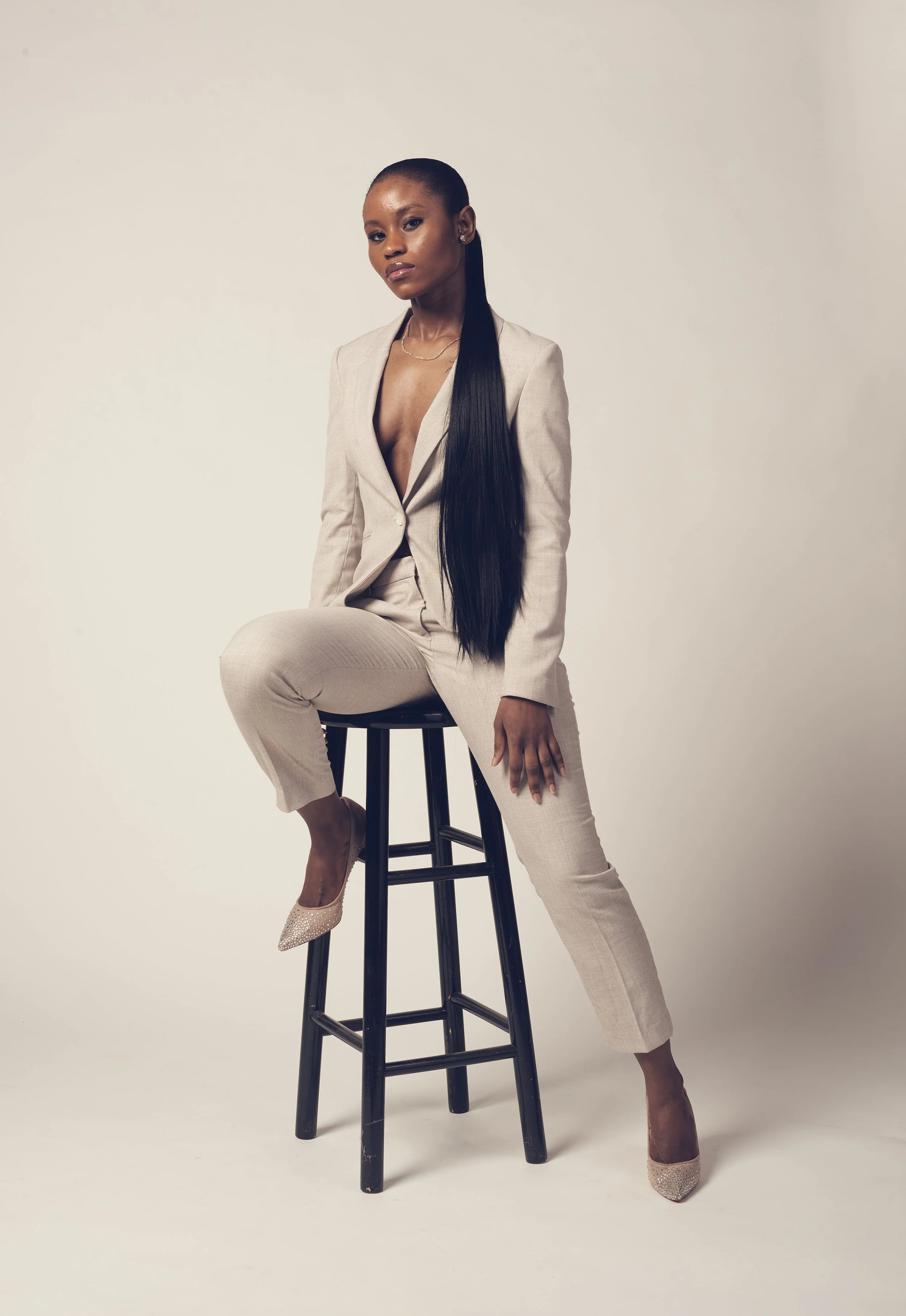 fashion photo shoot image of woman on black stool wearing grey business suit