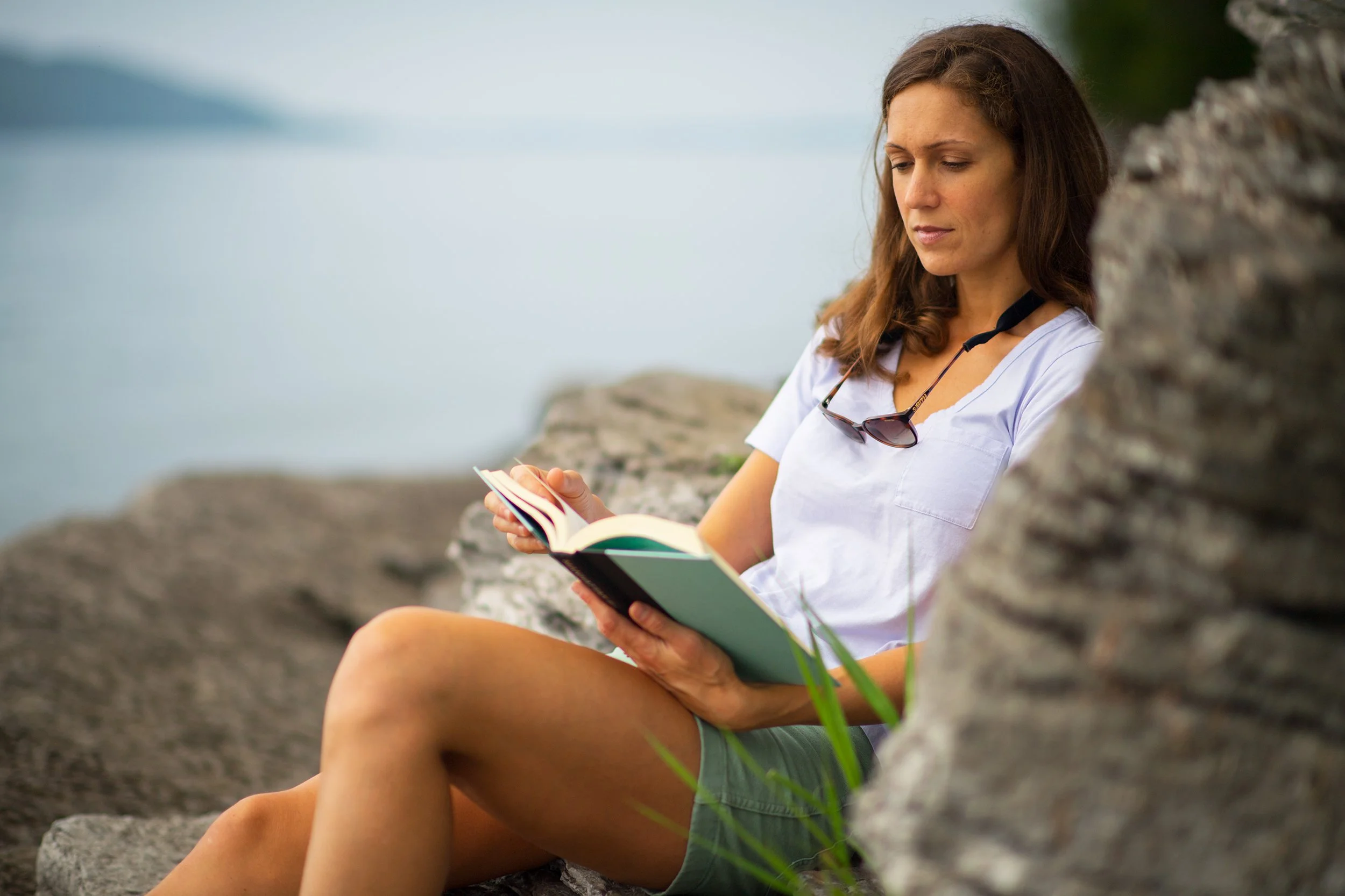 lifestyle photography of a woman reads a book while sitting on a rocky lake champlain vermont beach