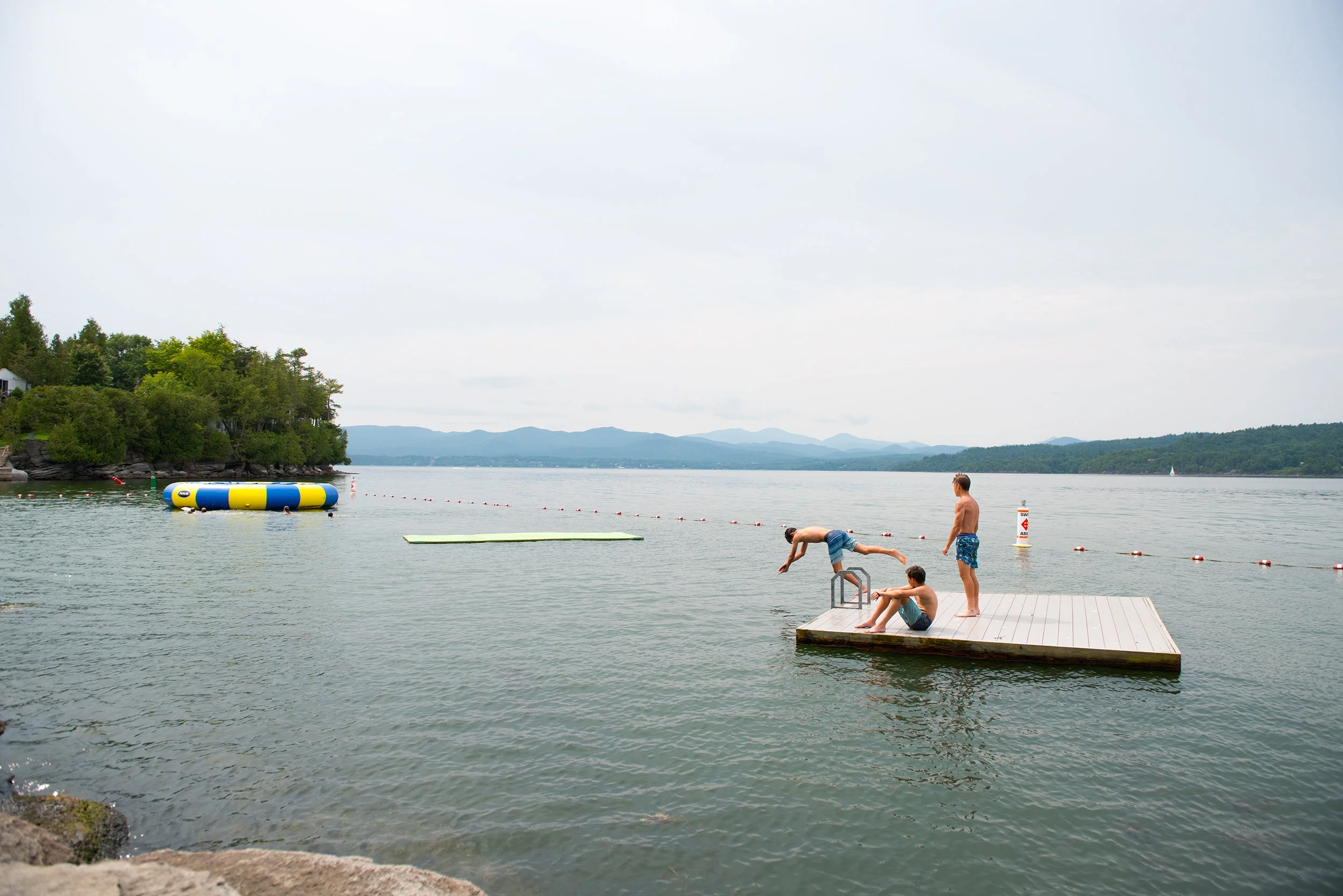 one boy dives off of a floating swim platform while his two friends look on