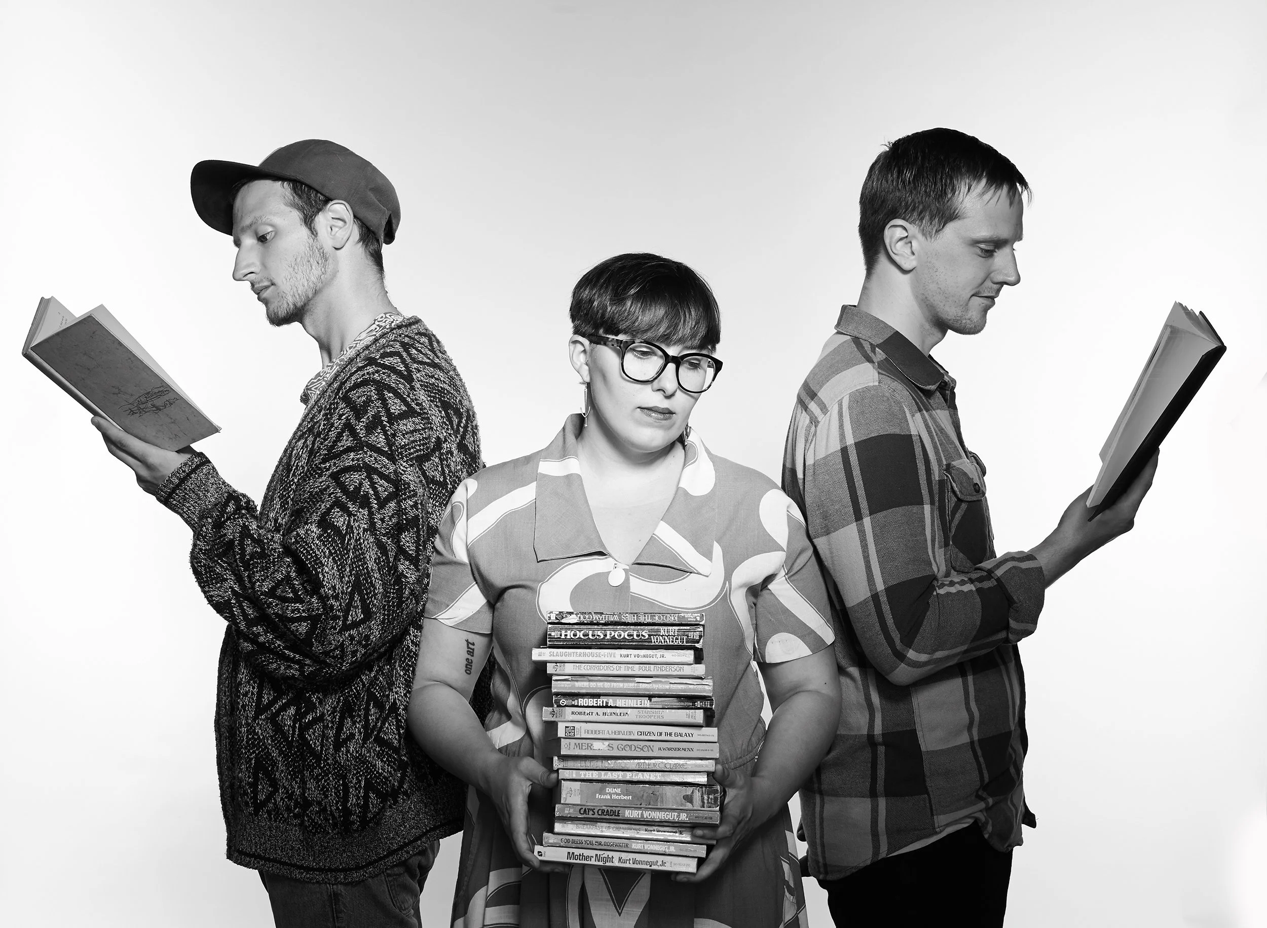 a woman holds a stack of books while her two bandmates read books on either side of her