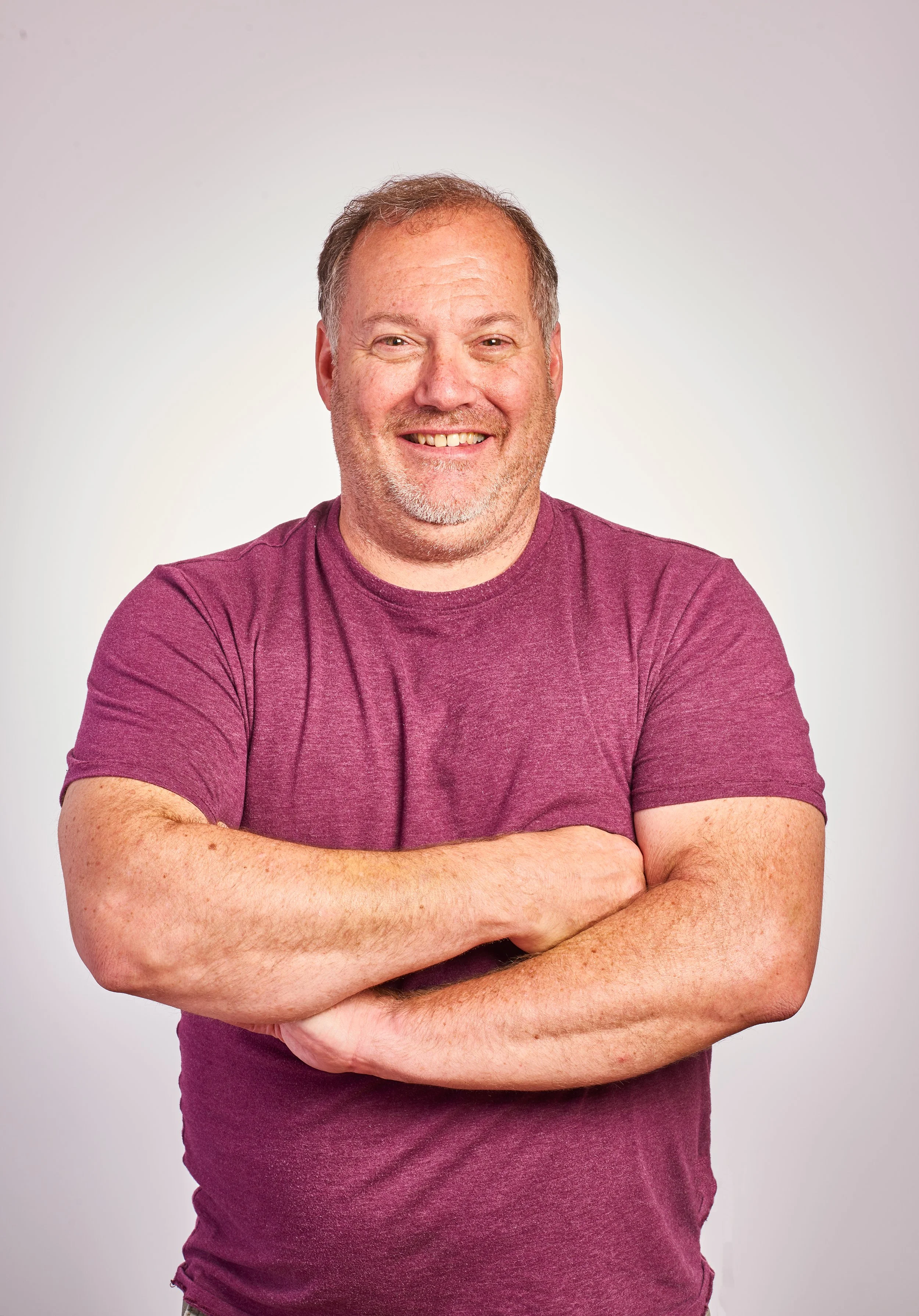 smiling man poses for a headshot with his arms crossed