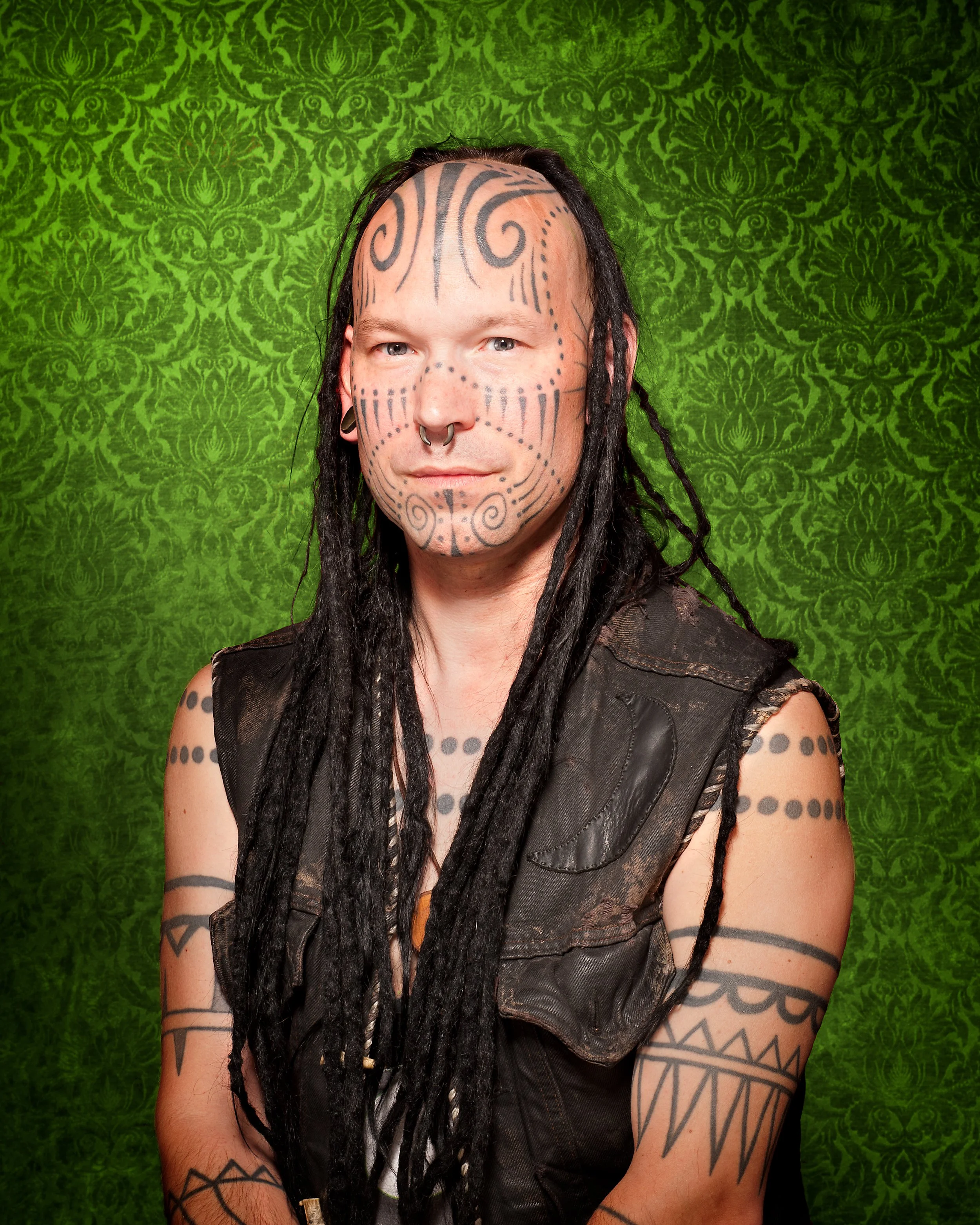 studio portrait of a tattooed man in front of a green background