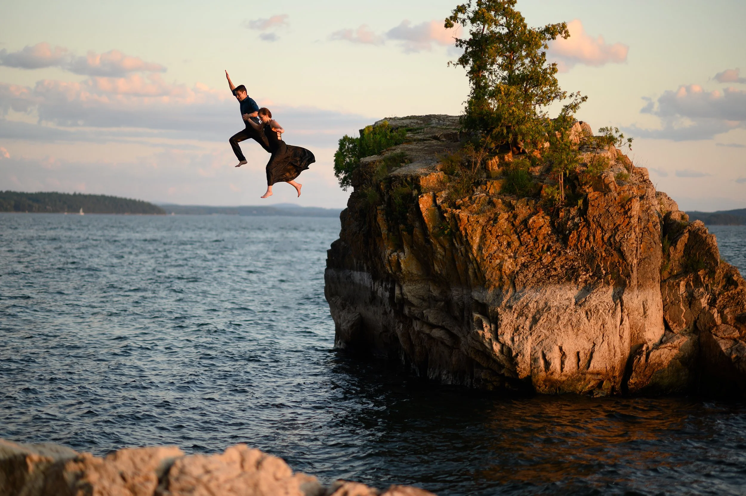 man and woman dressed in fancy black suit and dress jump off of lone rock in lake champlain vermont