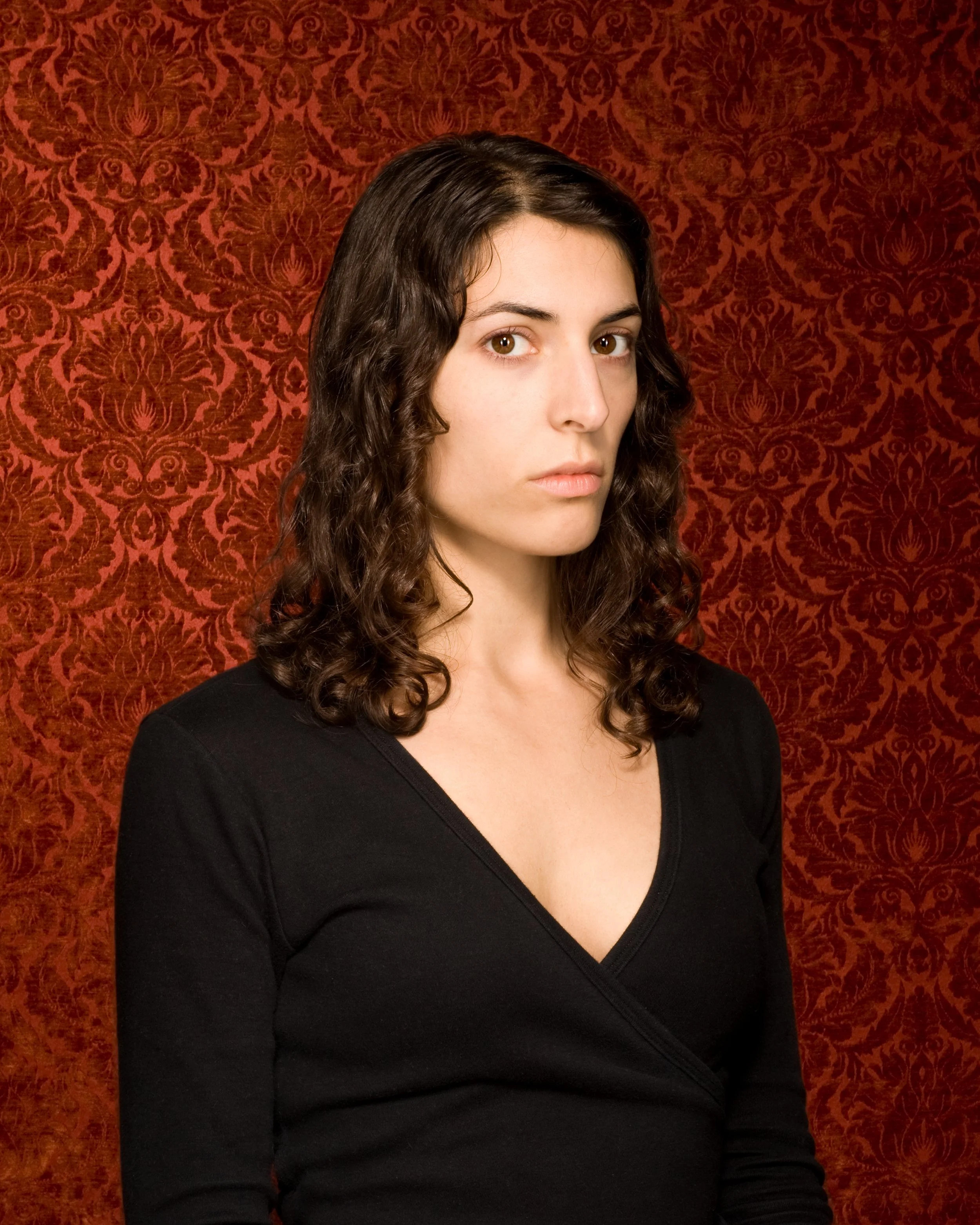 studio portrait of a woman wearing black in front of red damask background