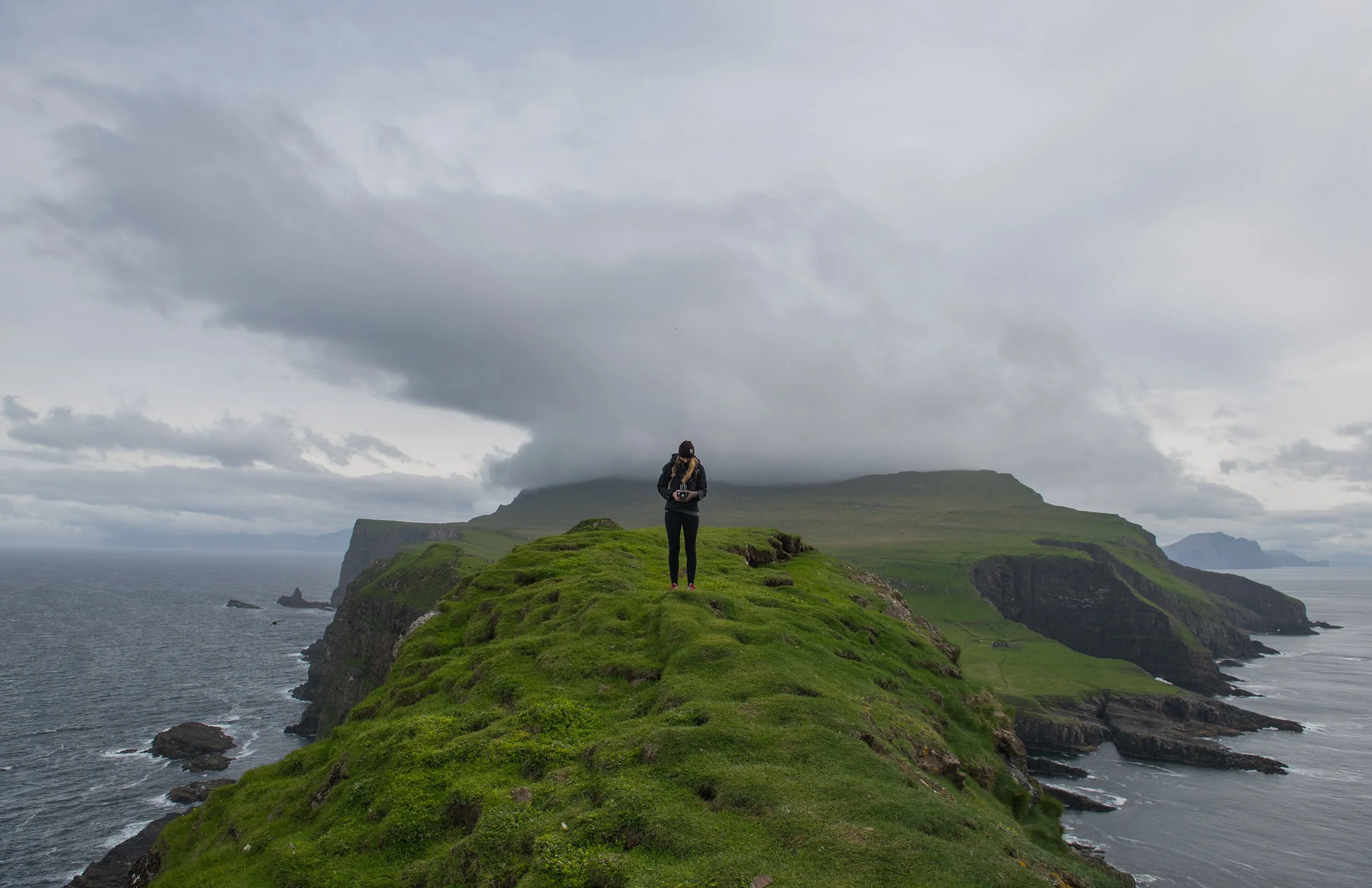 woman with a camera stands on top of the faroe islands