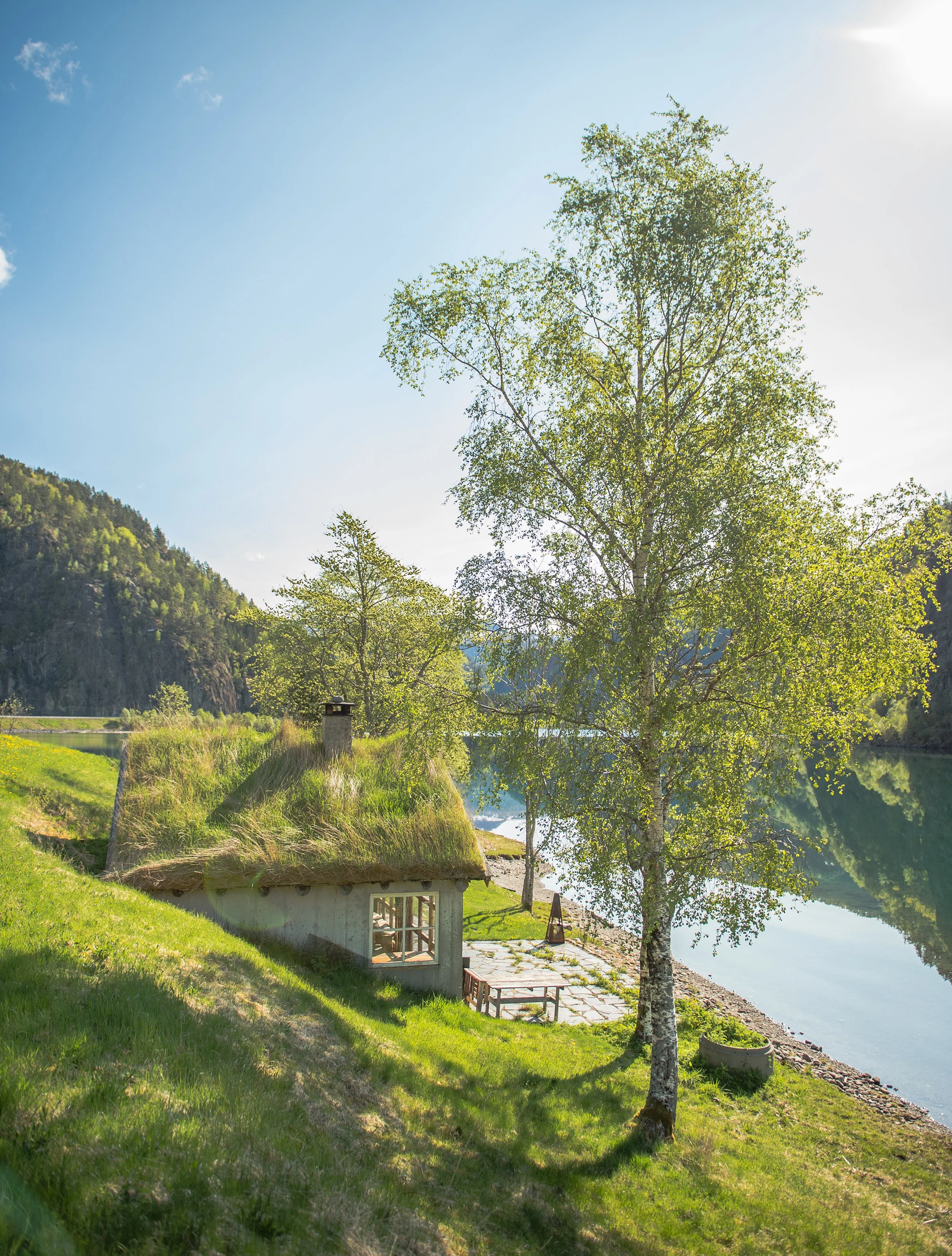 a sod roof house next to a lake on a sunny day in norway