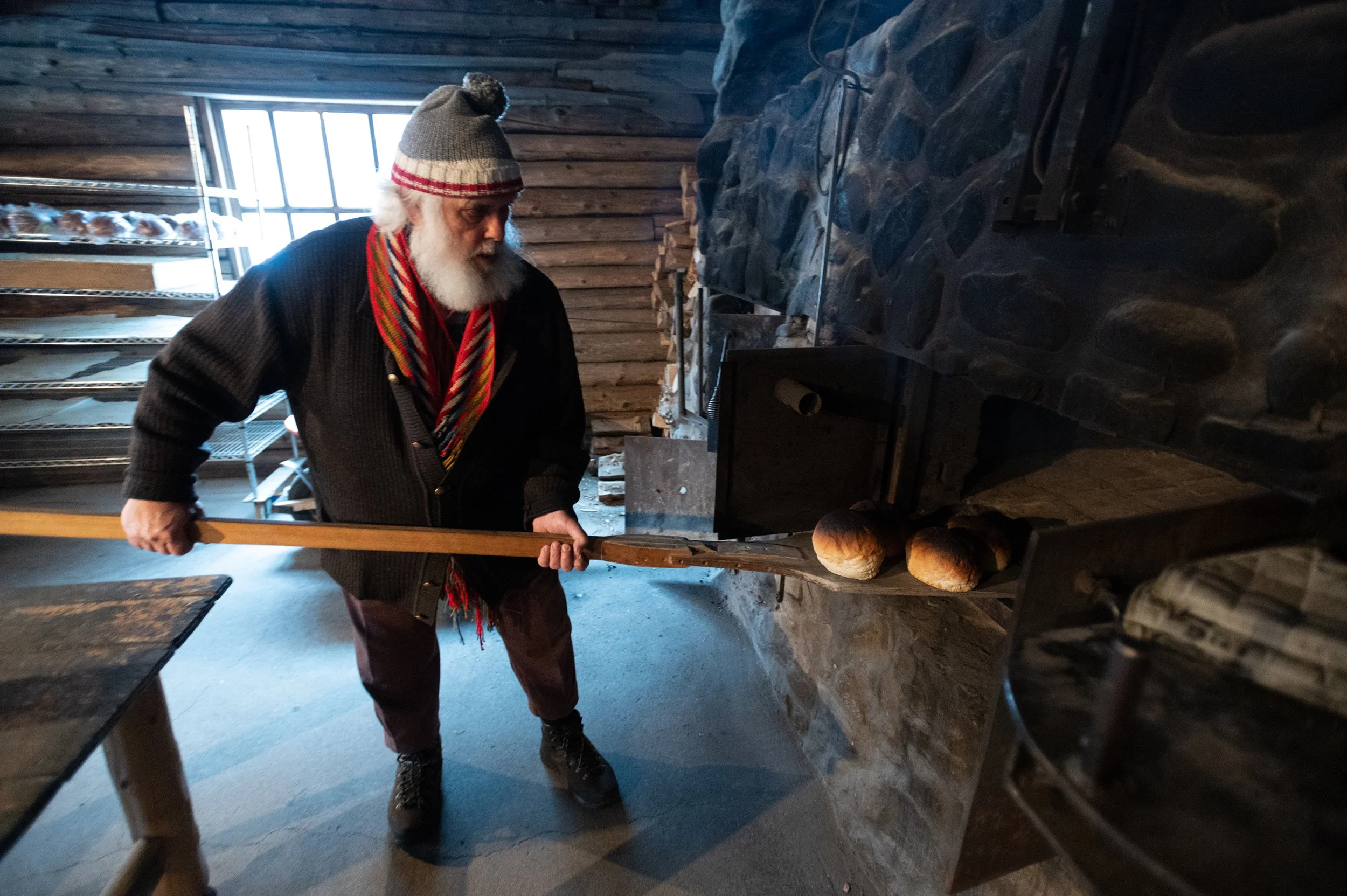 man with white beard and red scarf bakes bread in a wood fired oven 