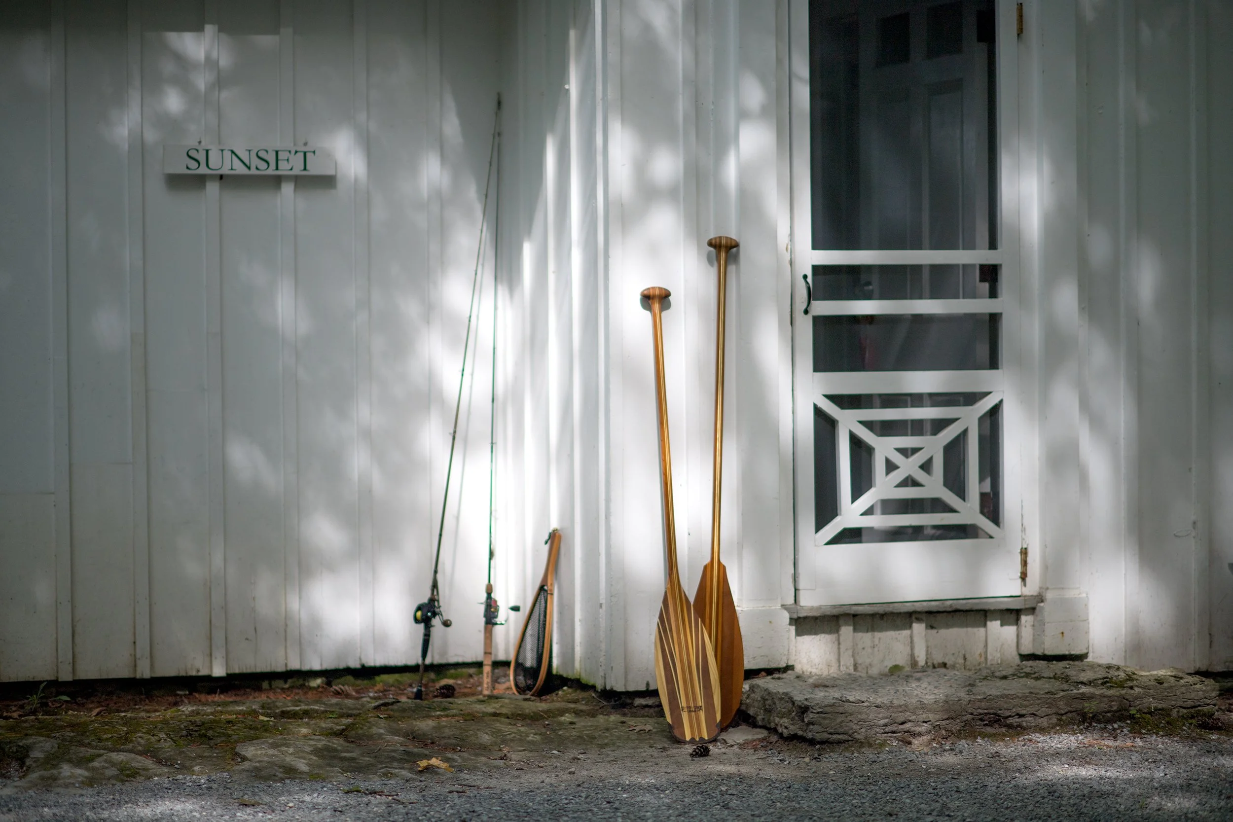 two fishing rods, a fish net, and two wooden paddles lean up against a cottage at basin harbor club in vermont