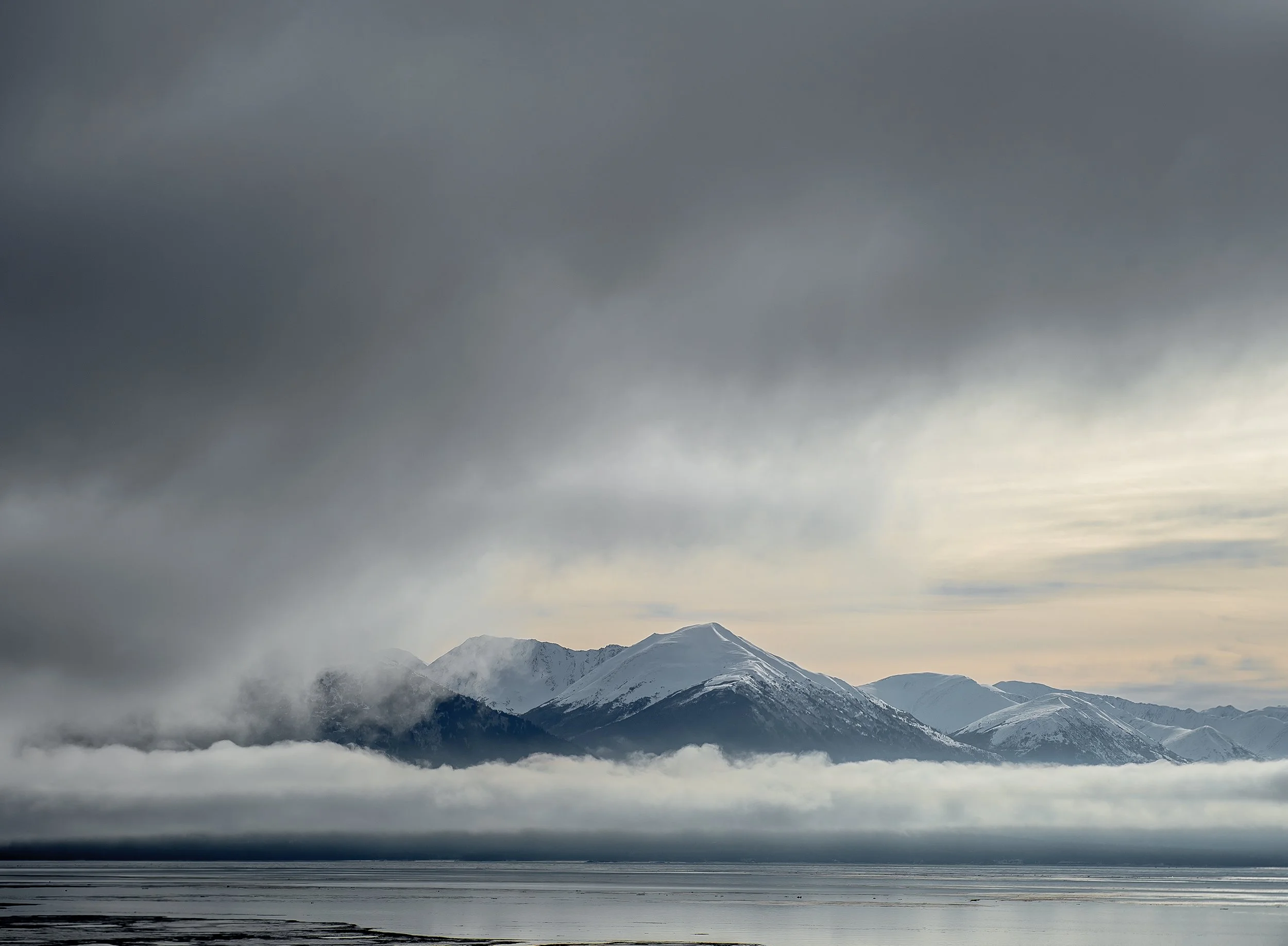 landscape photography view of an alaskan mountain with water in the foreground and dramatic gray cloudy skies