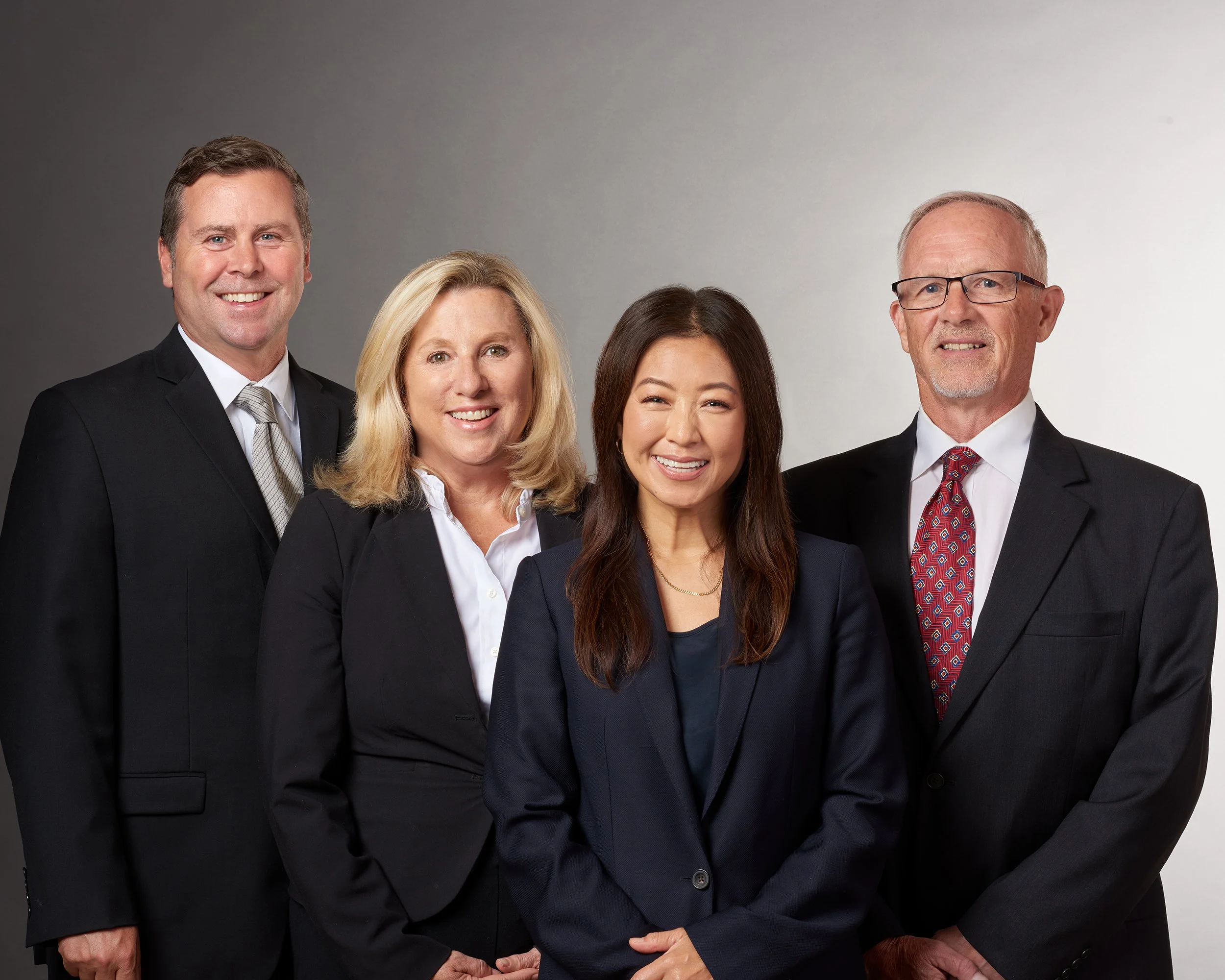 four financial advisors pose for a group portrait in front of a grey background