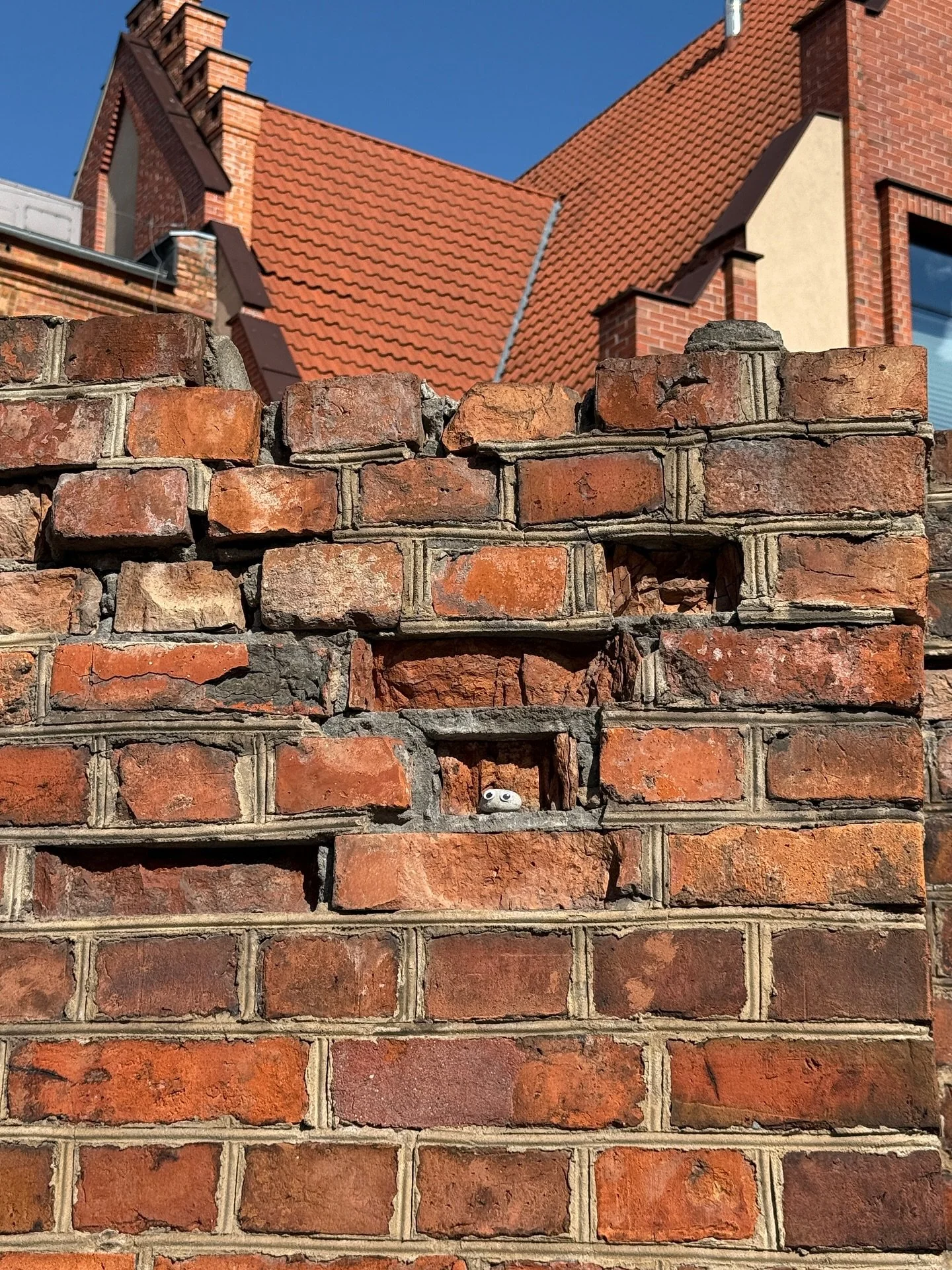 This image shows a damaged historic brick wall where hard cement mortar was used in previous repairs &mdash; a common but harmful mistake in restoration.

The cement mortar is much harder and less porous than the original historic bricks (which were 