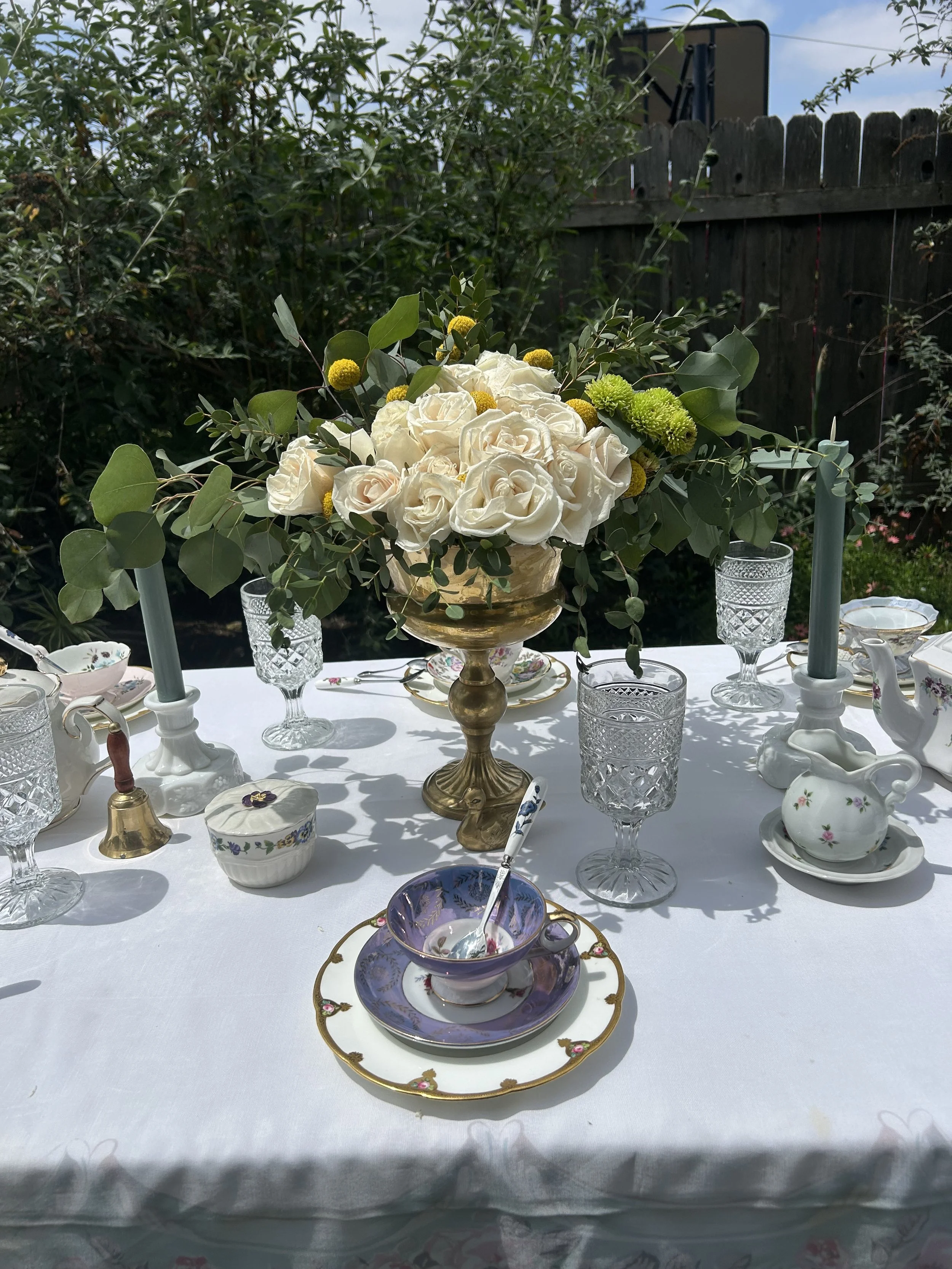 Elegant outdoor table setting with vintage tea cups and floral centerpiece.