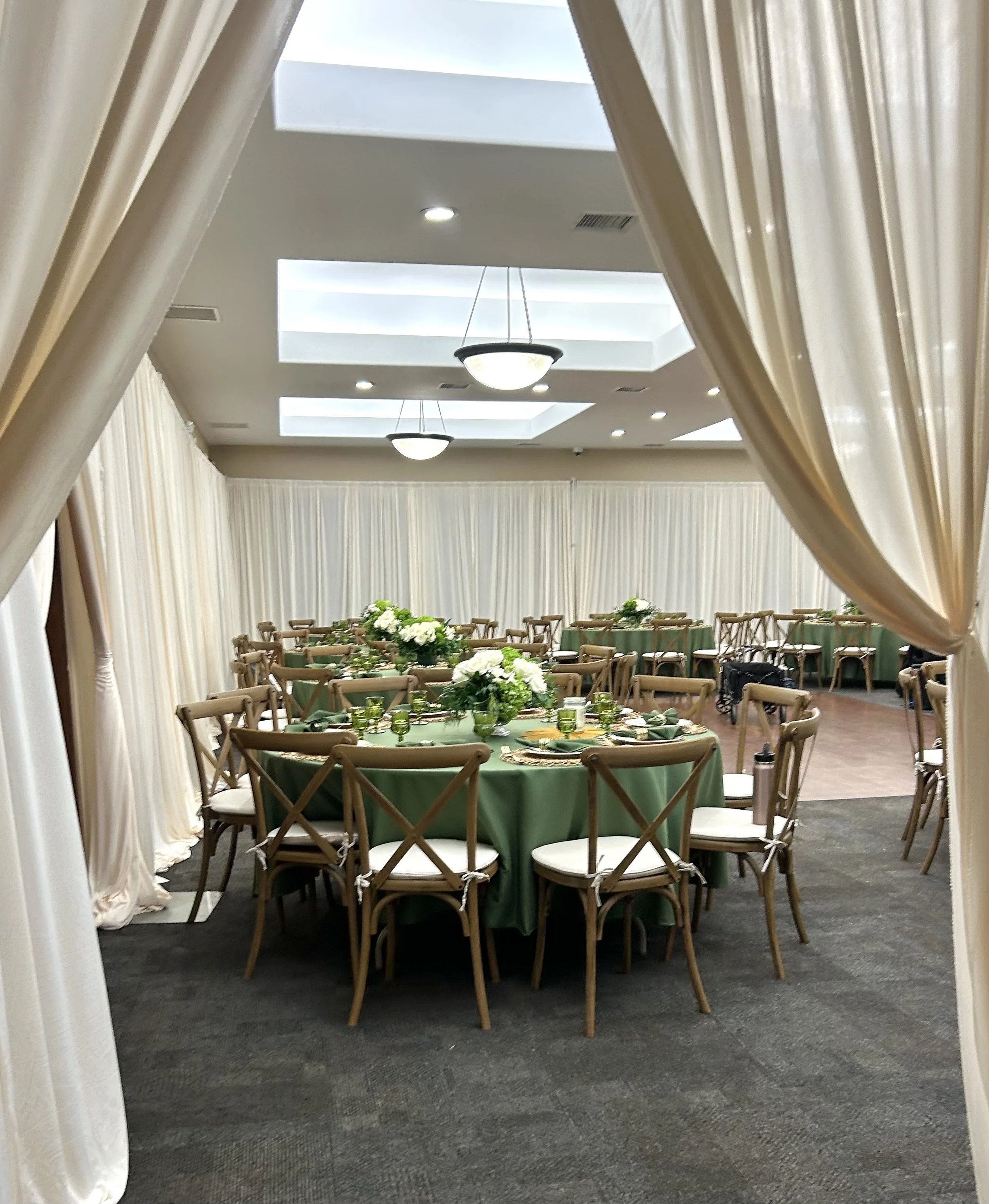 Elegant banquet hall with round tables decorated with green tablecloths and floral centerpieces, seen through a curtain
