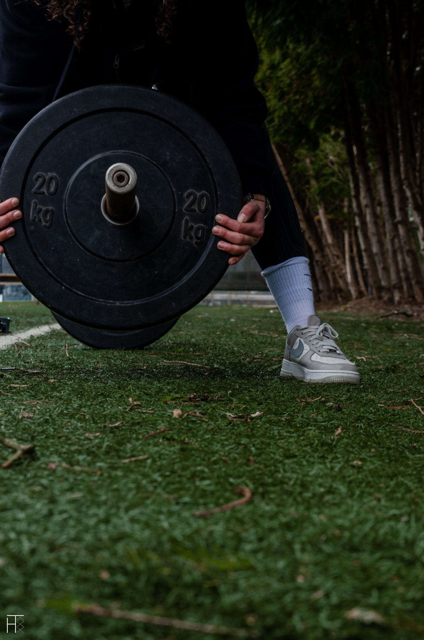 Person holding a 20 kg weight plate on a grassy field