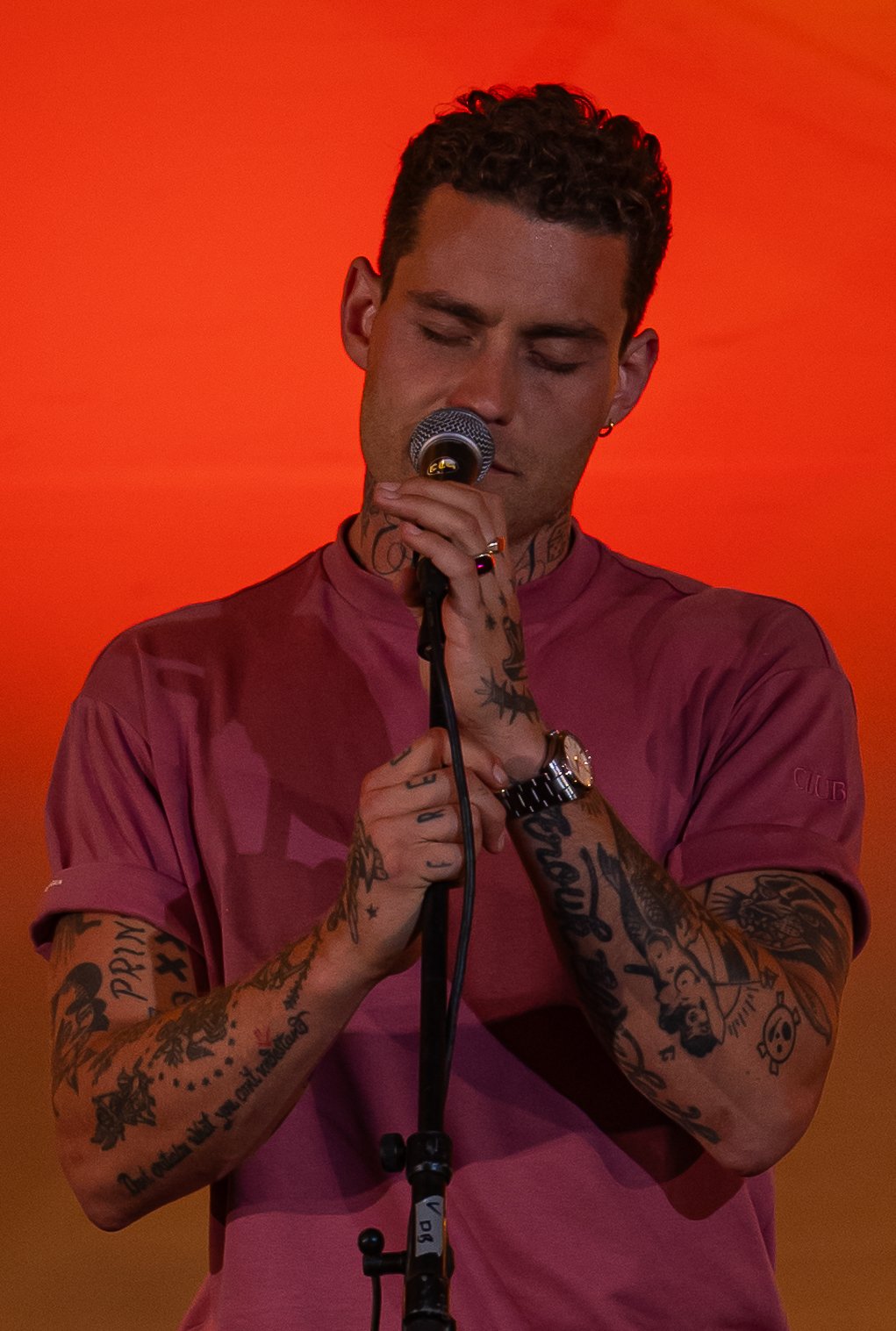 Tattooed singer with microphone against red background