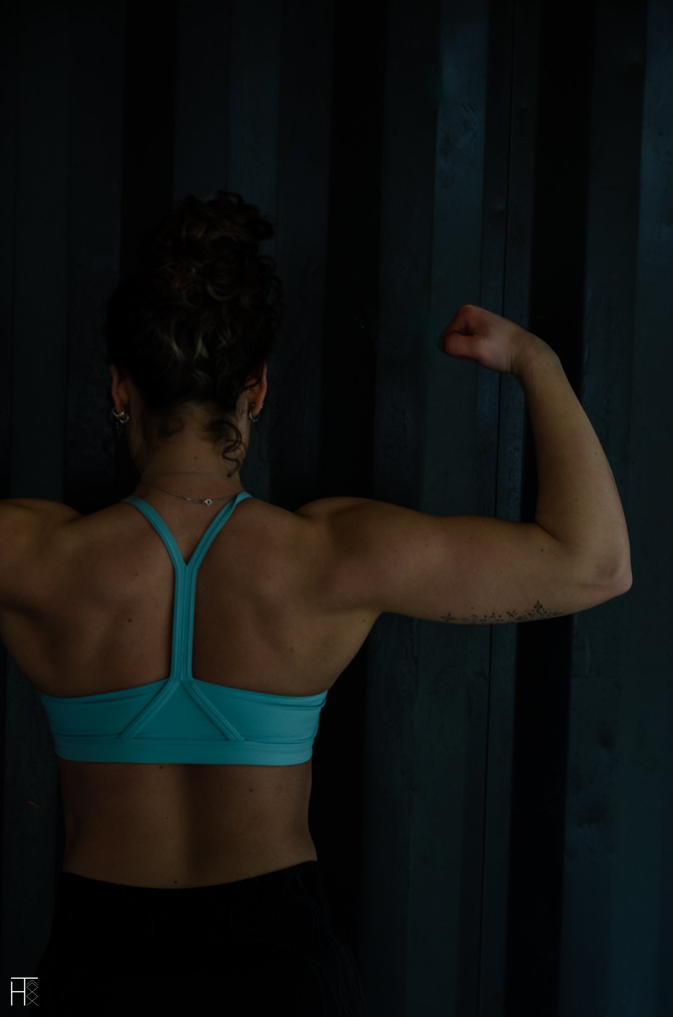 Person in sportswear flexing arm in front of a dark background.