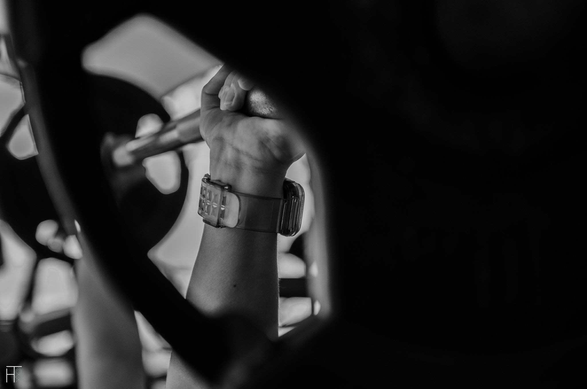 Black and white photo of a person lifting a barbell with plates in a gym, wearing a wristwatch.