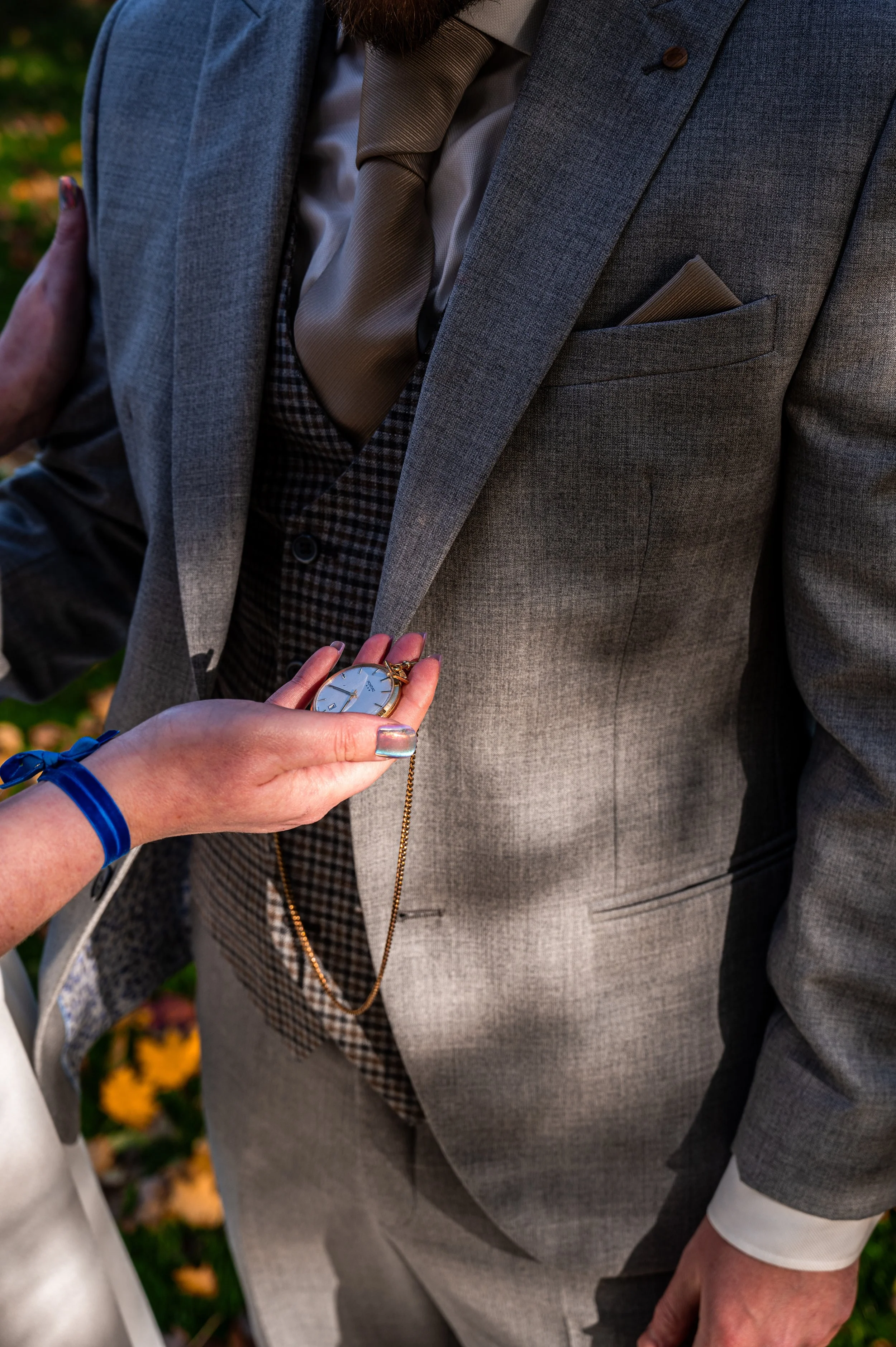 Persoon in grijs pak die een zakhorloge ontvangt van een andere persoon met een blauwe polsband.