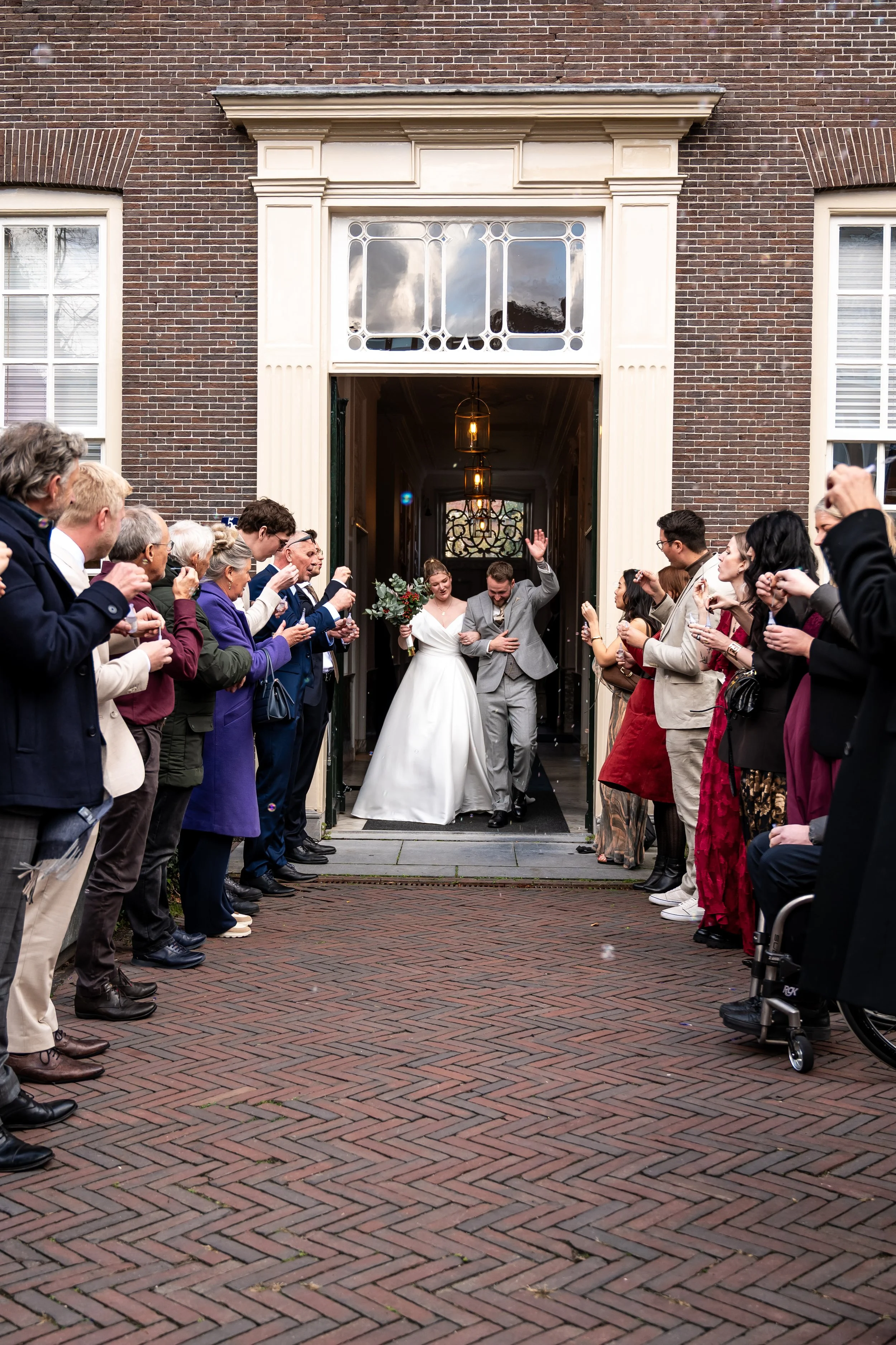 Gelukkige bruid en bruidegom die de gebouwen uitgang verlaten terwijl gasten hen toe juichen en applaudisseren.