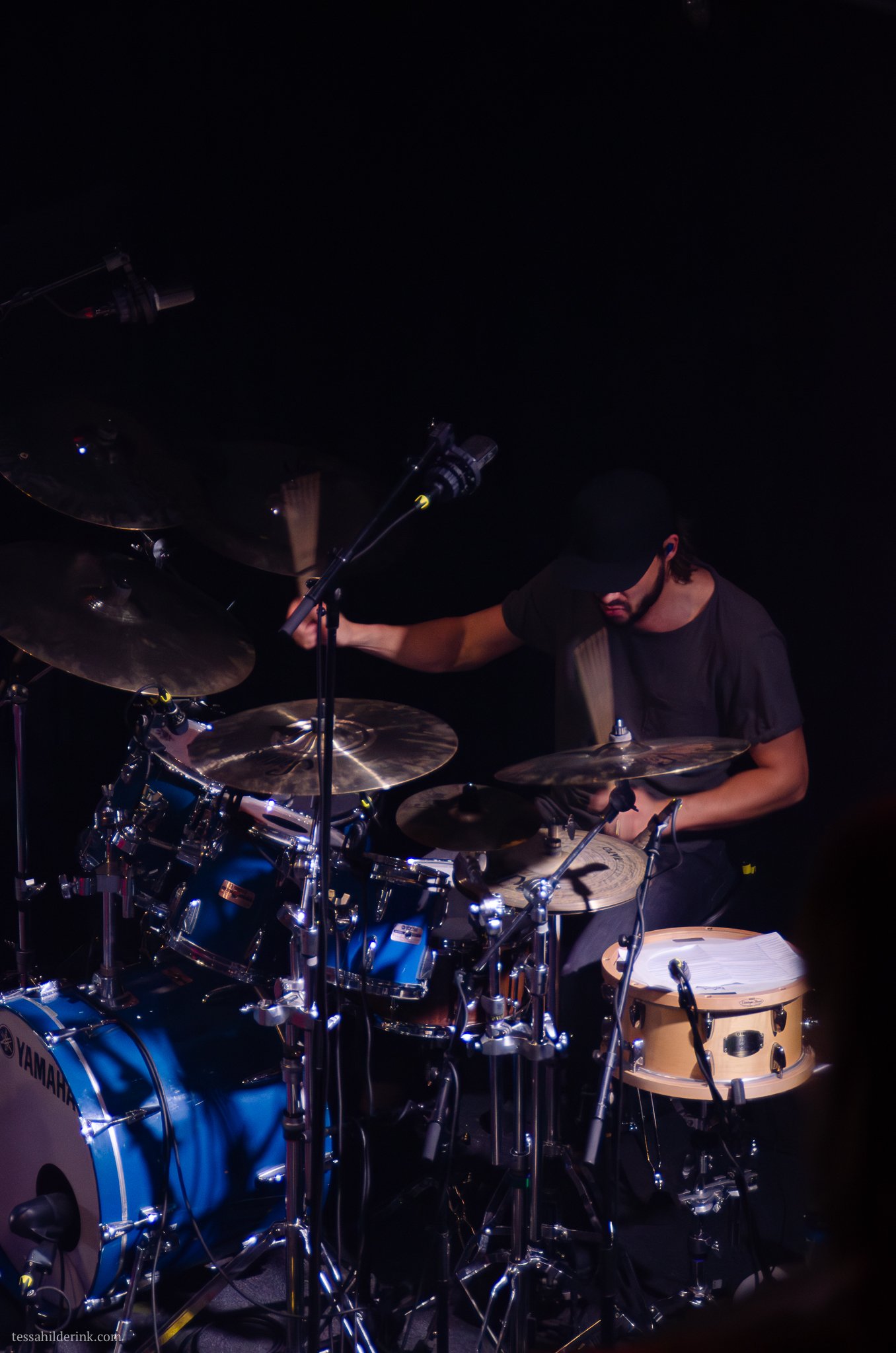 Drummer playing a blue drum set with cymbals and microphones.