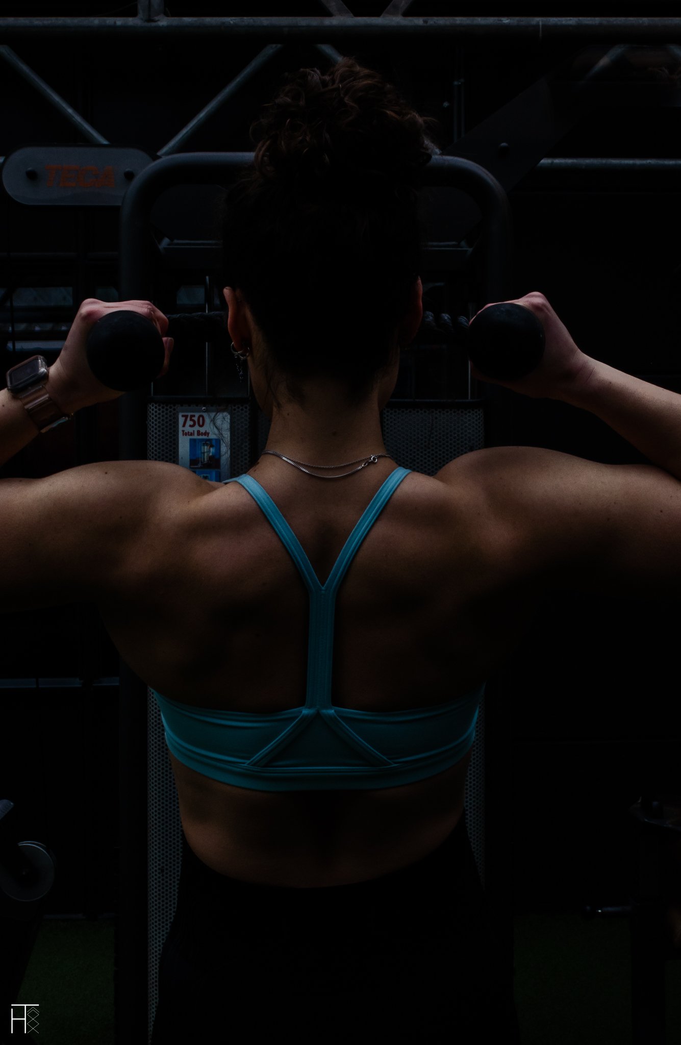 Person exercising on gym equipment, wearing a blue sports bra, viewed from the back.