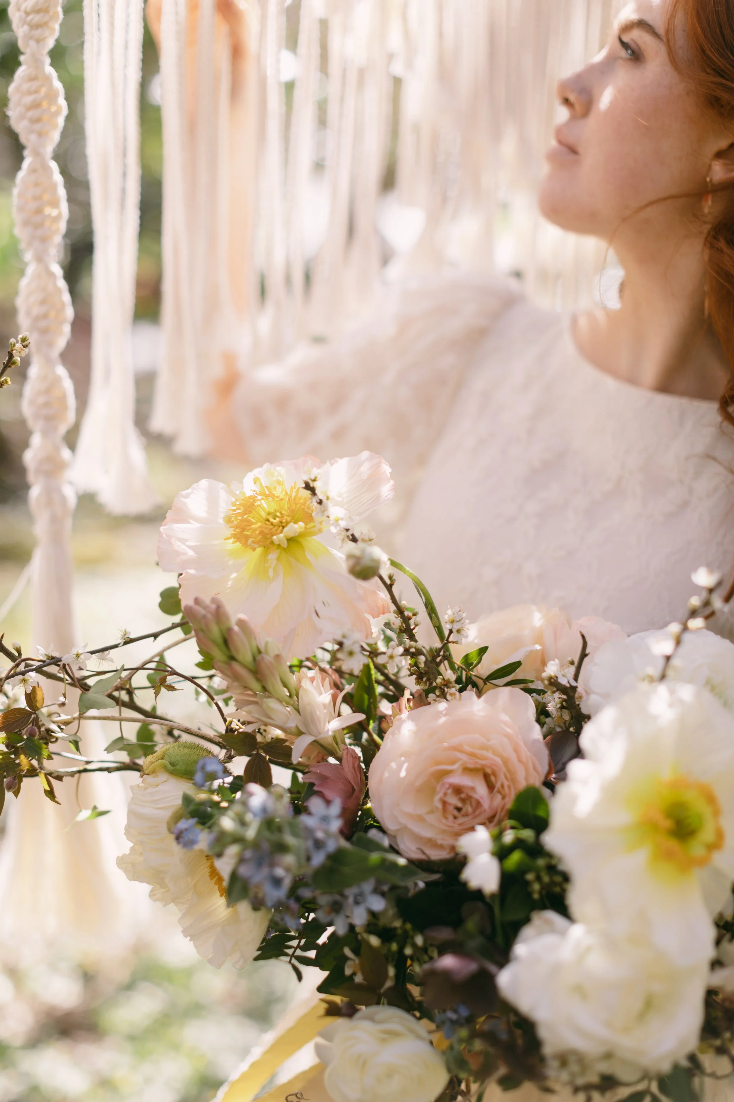 Close-up of a wedding bouquet with white, pink, and purple flowers, with a woman in the background.