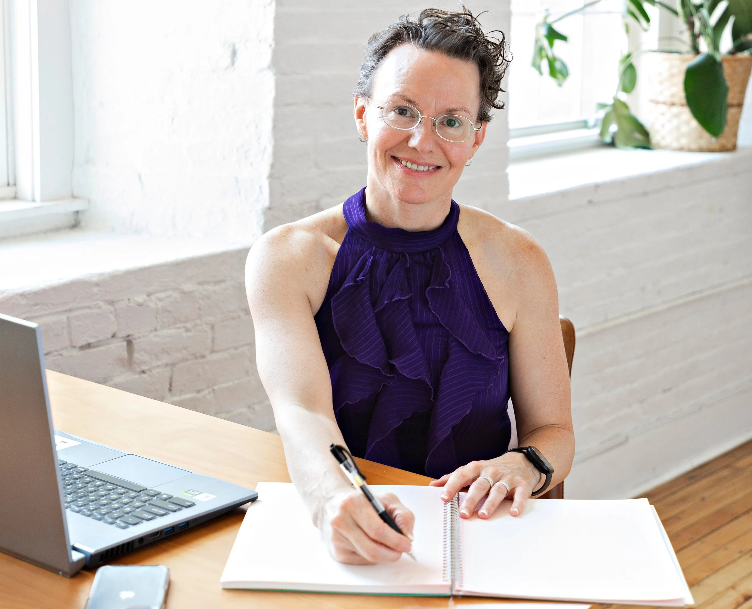Stephanie smiling at the camera with a pen in hand over an open journal, representing reflection, self-awareness, and taking action toward improved gut health.