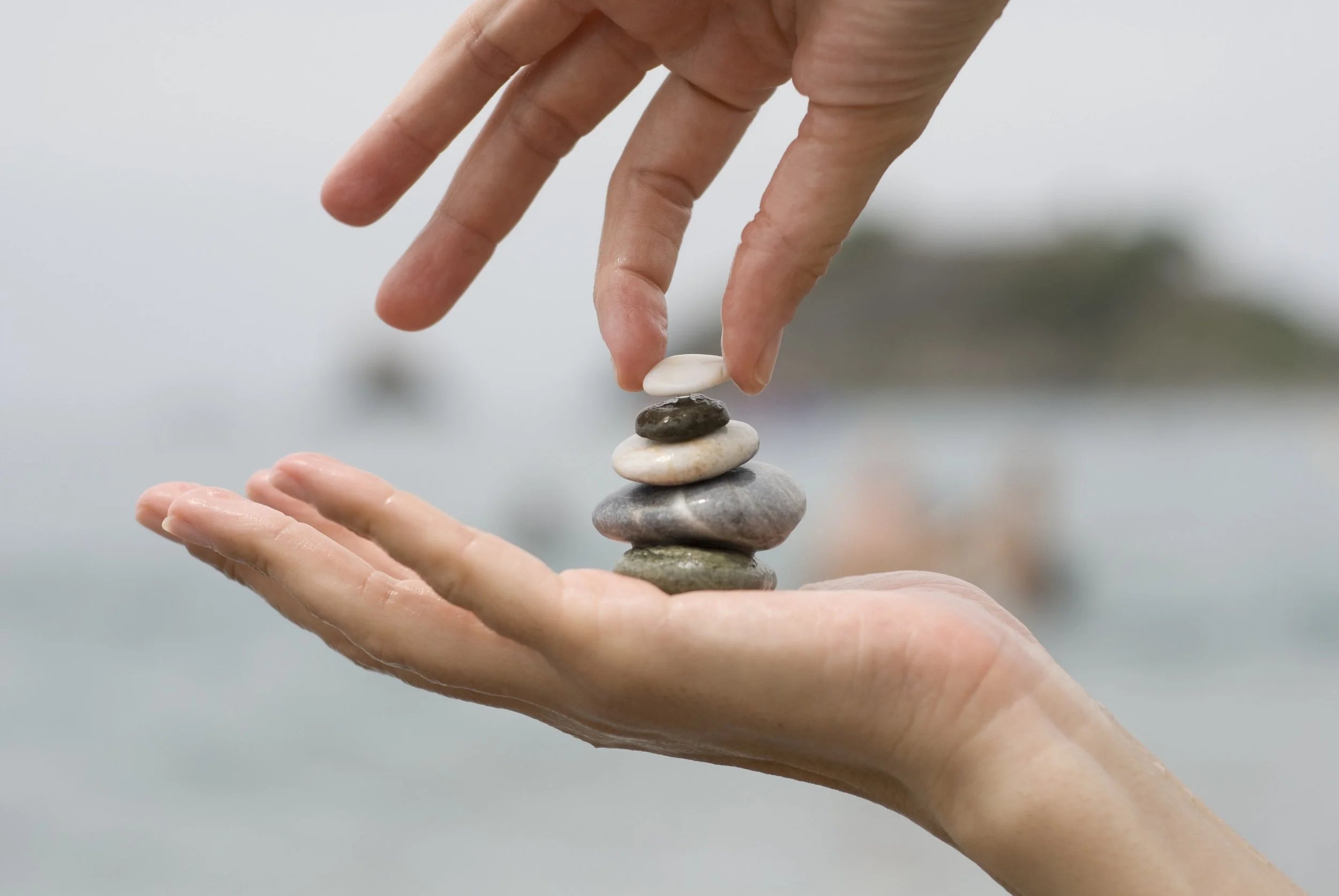 A hand carefully placing the final rock on a balanced stack, symbolizing the Balance phase of the 12-Week Gut Health Program where participants create balance in food choices, energy, and lifestyle habits.