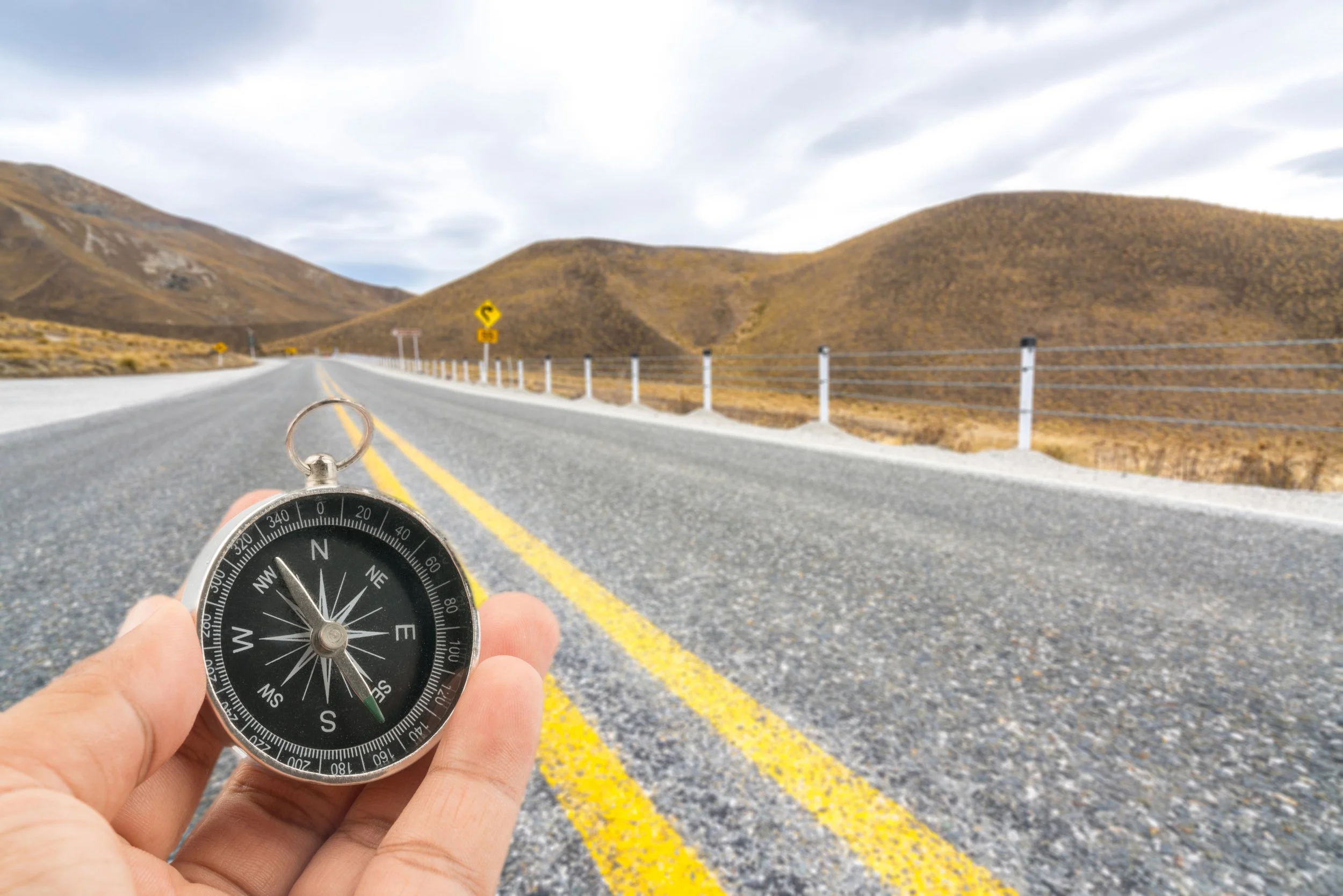 A hand holding a compass with a road stretching ahead, representing the Curiosity phase of the 12-Week Gut Health Program where participants explore their unique gut health journey and discover what works for their body.