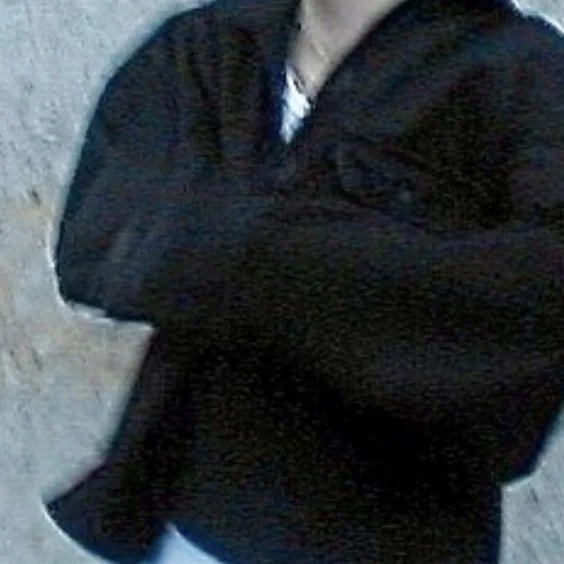 Christopher Clucas in a black jacket crossing arms, standing outdoors near a textured wall