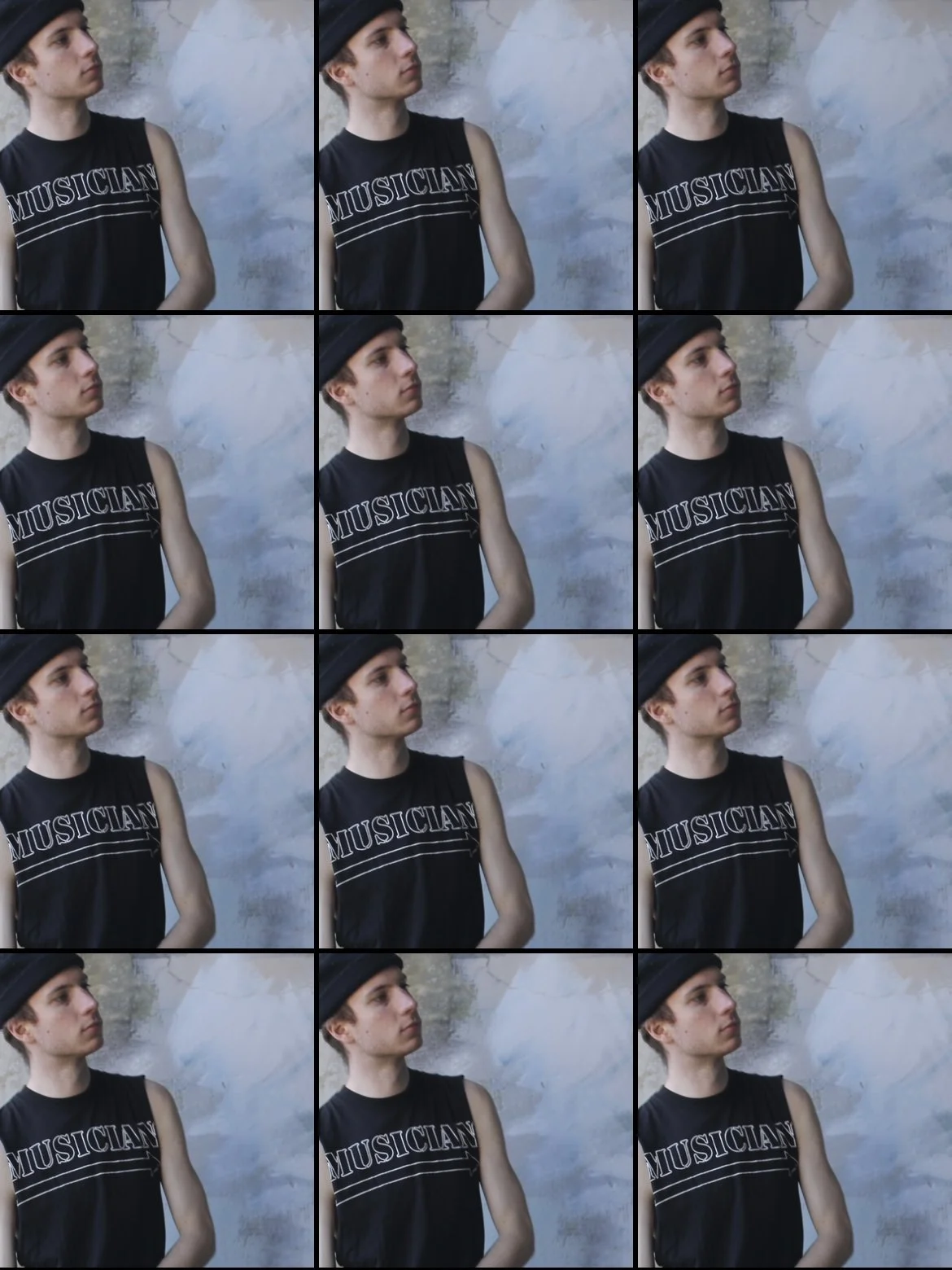 Christopher Clucas wearing a black sleeveless shirt with the word 'MUSICIAN' printed on it, and a black hat, standing outdoors against a textured wall. The person is looking slightly to the right with a neutral expression.